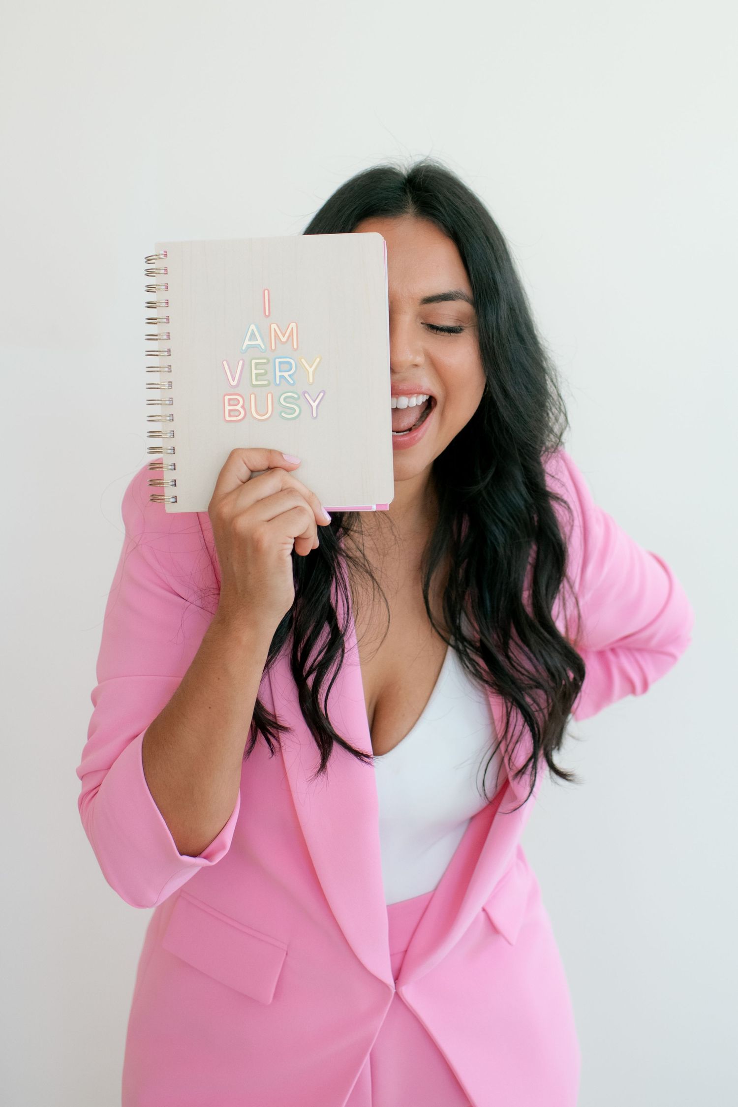 Person in pink blazer holding notebook with joyful expression against white background.