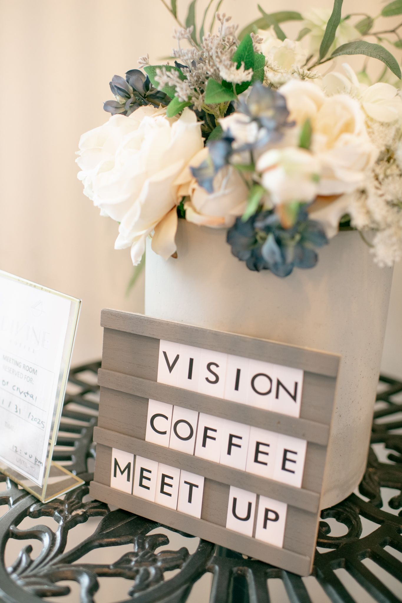 Decorative white floral arrangements with Scrabble-style letter signs spelling words like 'COFFEE' and 'VISION' on gray stands.