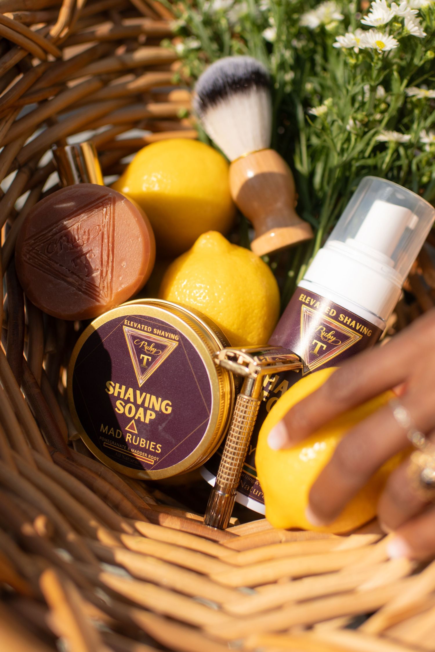 Wicker basket with Made Rubies shaving soap, razor, brush, beyond shaving foam, and fresh lemons with white flowers.