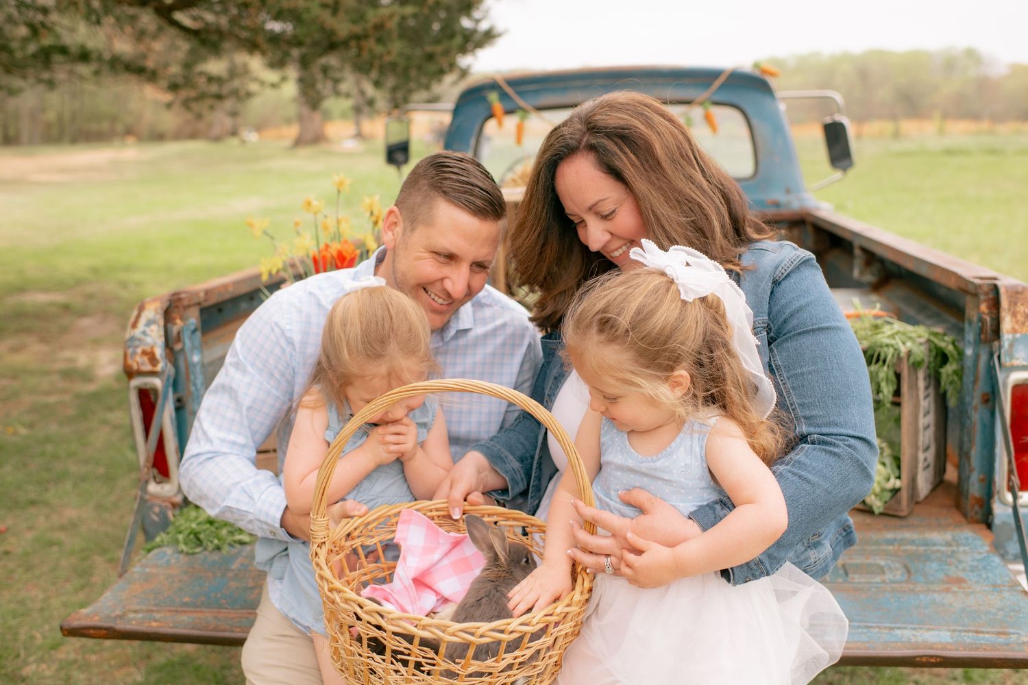 A happy family gathers around a wicker basket in the bed of a vintage turquoise pickup truck in golden sunlight.