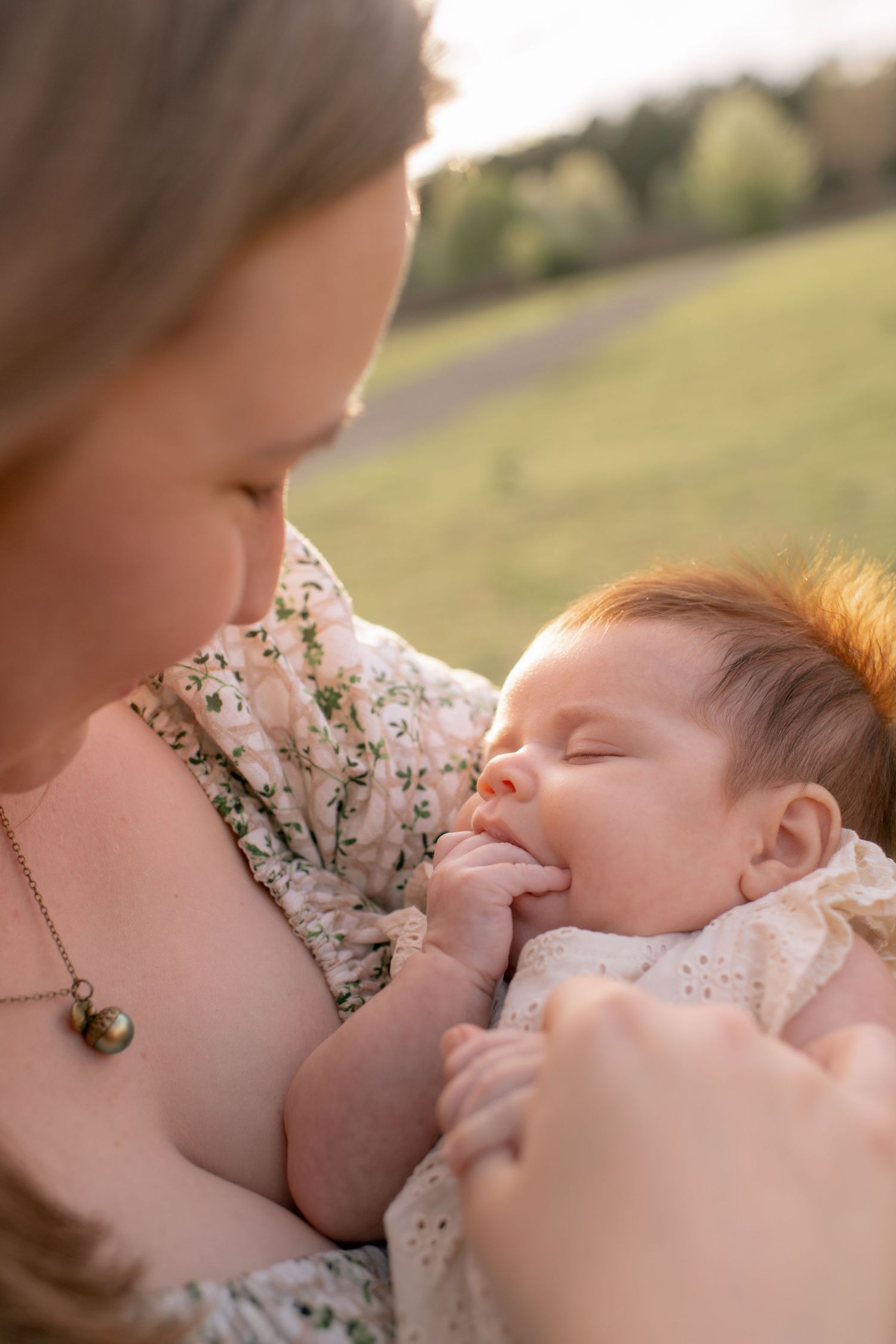 A peaceful moment captured outdoors as a mother cradles her sleeping infant in a floral dress on a sunny day.