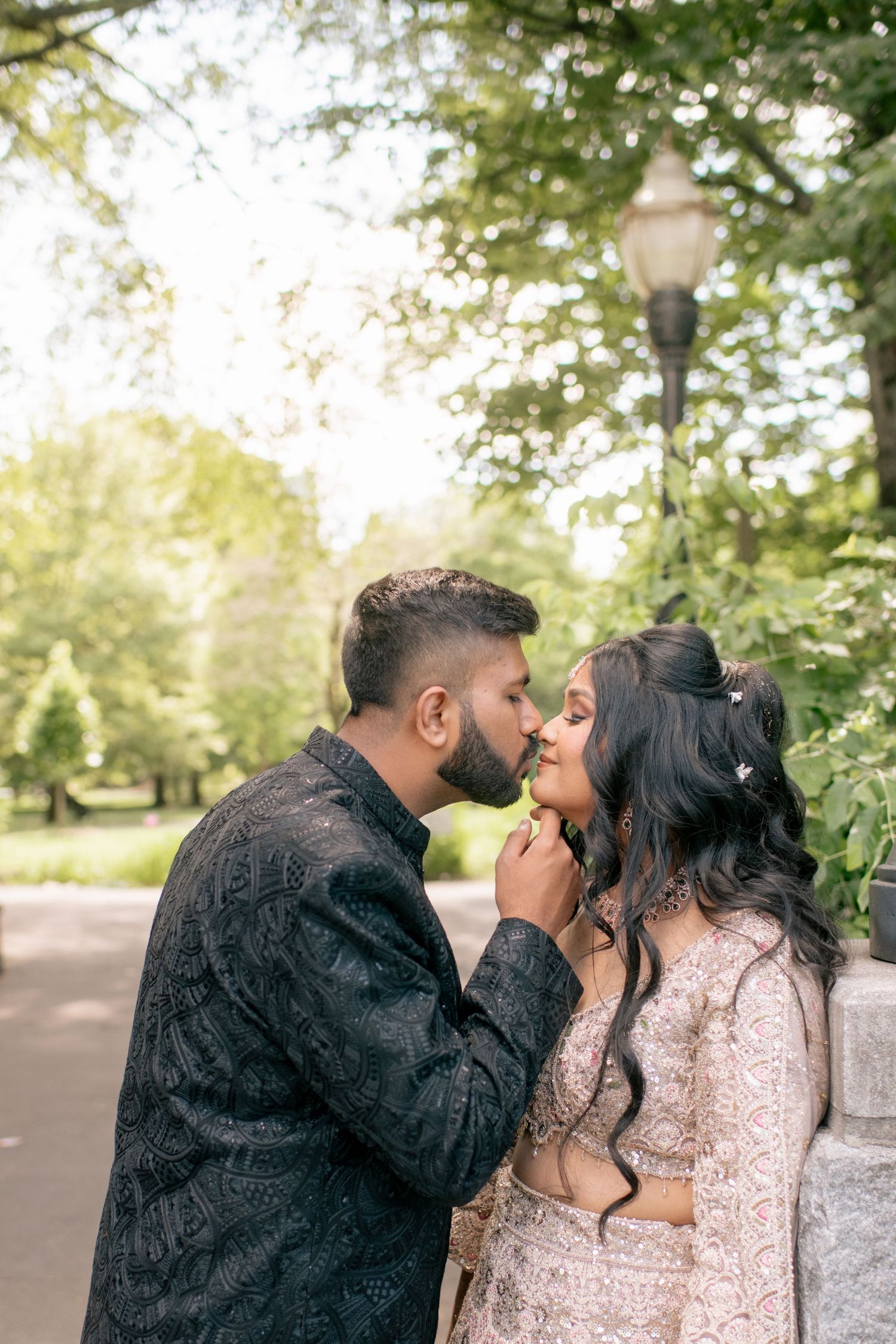 Romantic outdoor portrait of a couple in traditional South Asian wedding attire sharing an intimate moment.
