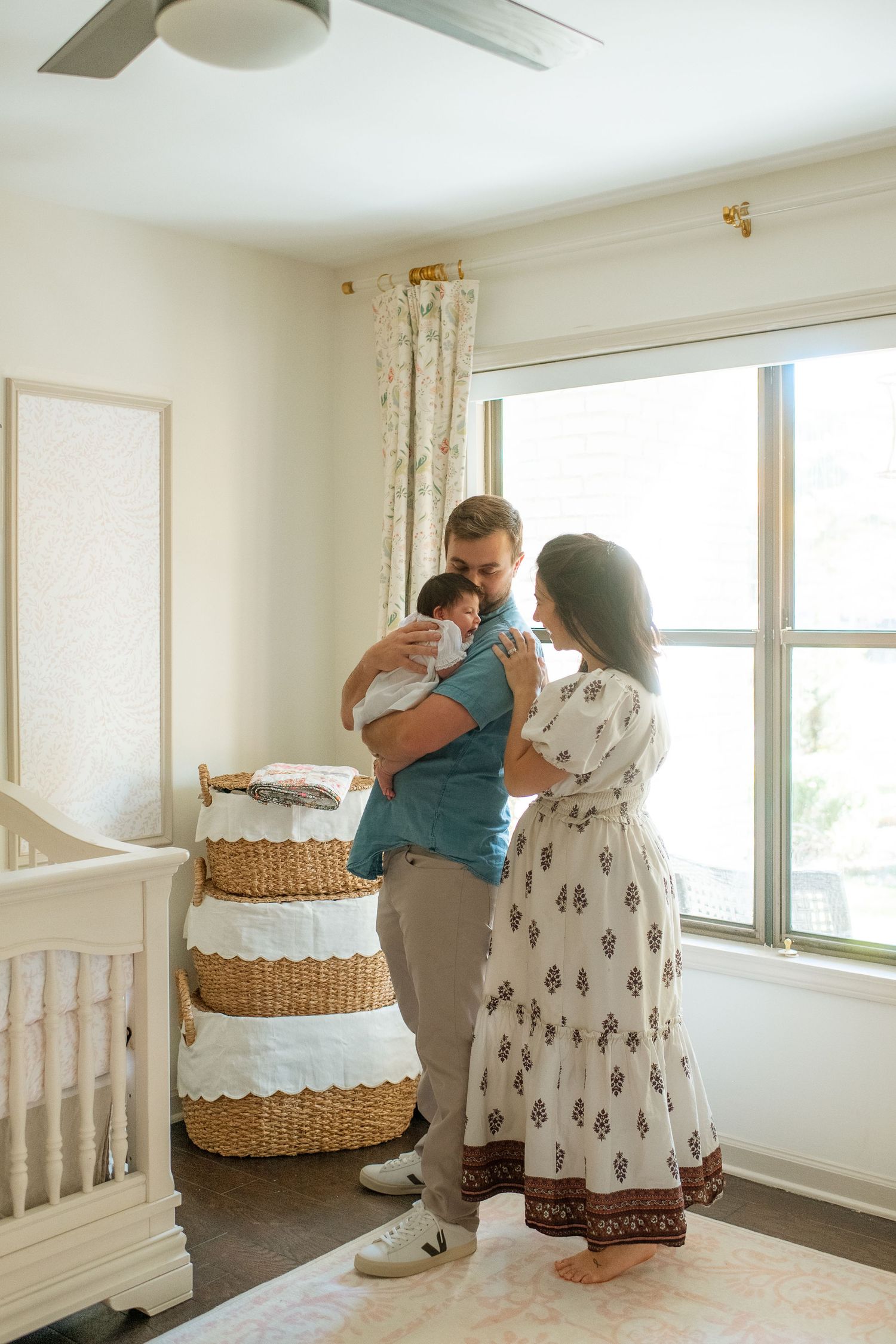 Family gathering around their newborn baby near a window with decorative baskets in the background.