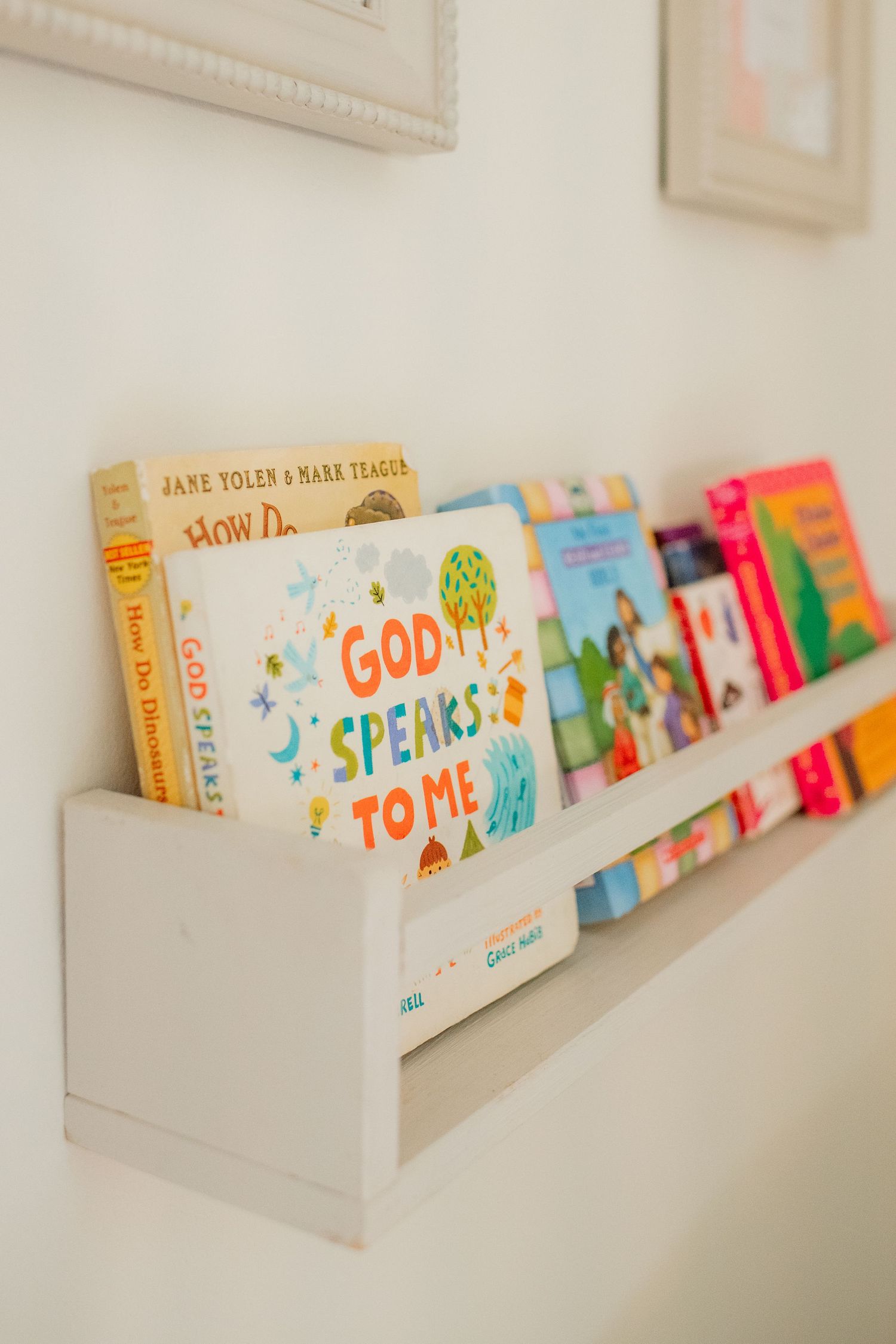 Colorful children's books displayed on a white floating wall shelf in a nursery.