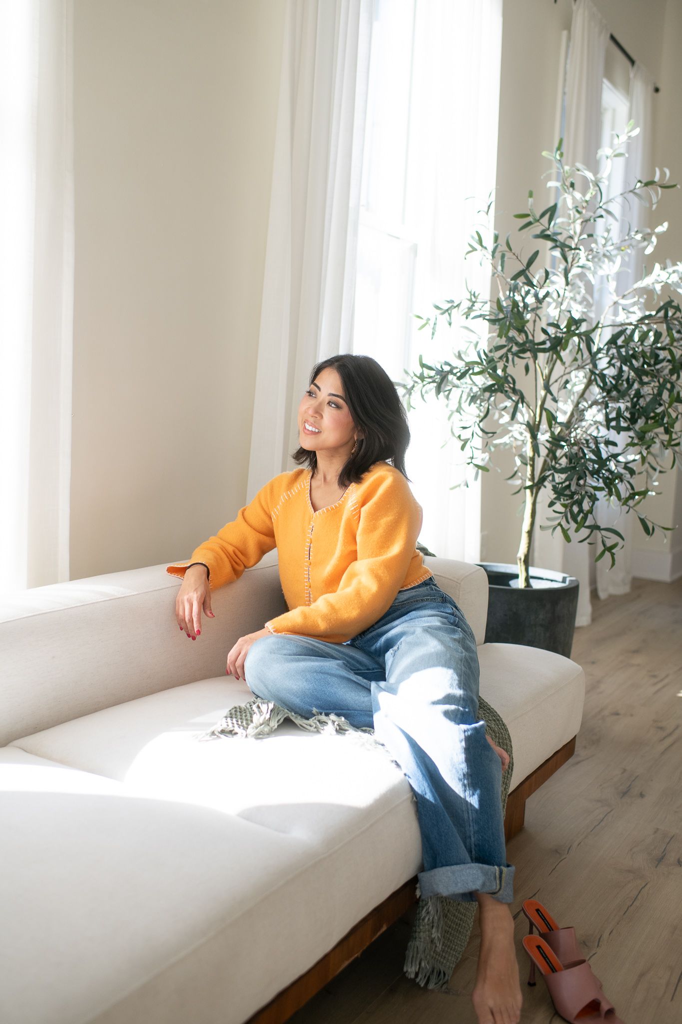 Person lounging on white sofa near windows in bright modern room with plants.