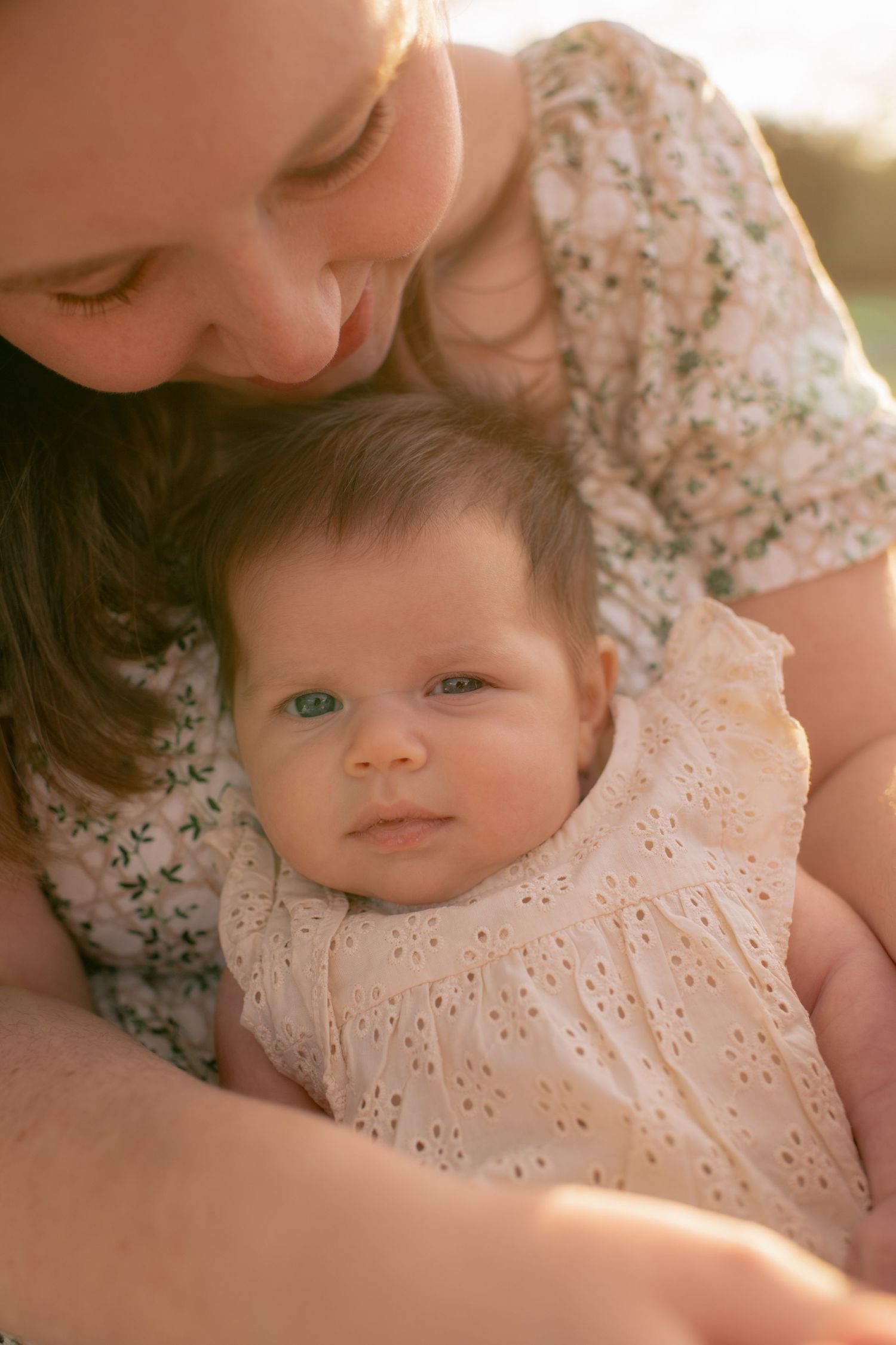 A tender moment between parent and baby in soft lighting, wearing delicate floral and eyelet lace clothing.