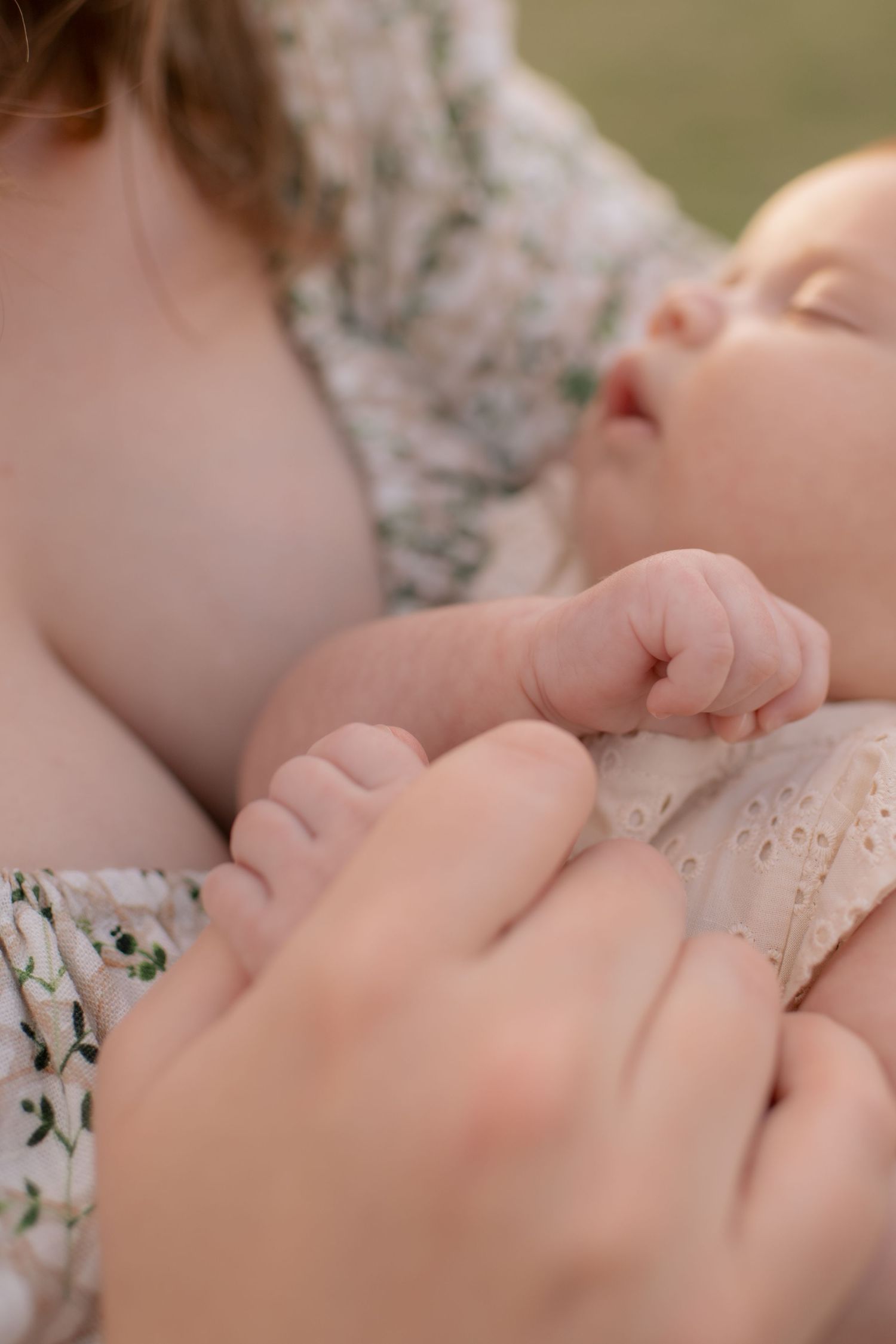 A tender close-up of a sleeping baby's tiny hand being gently held while resting against floral-patterned fabric.