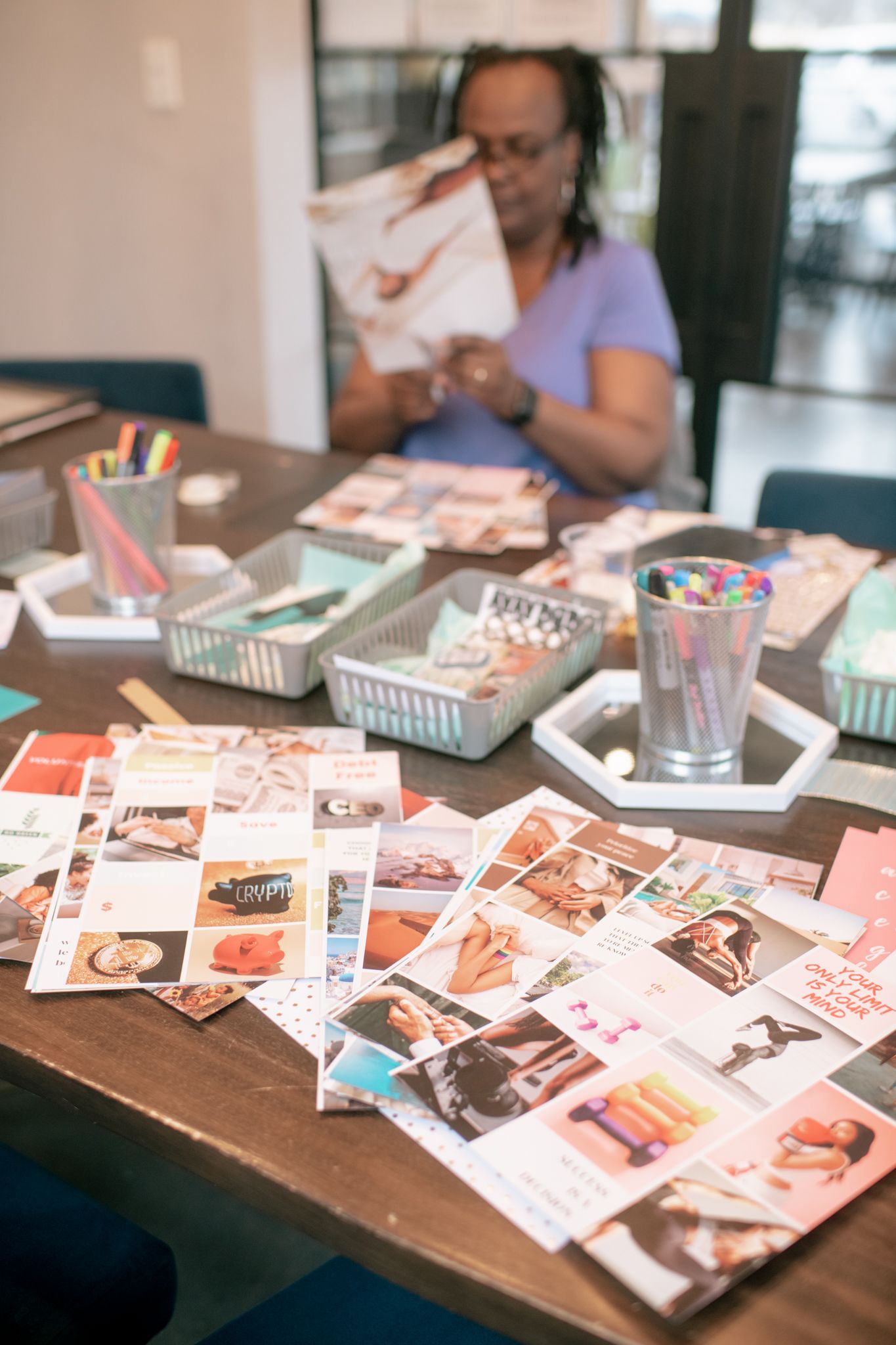 A table covered in photographs and craft supplies with someone looking through images in the background.