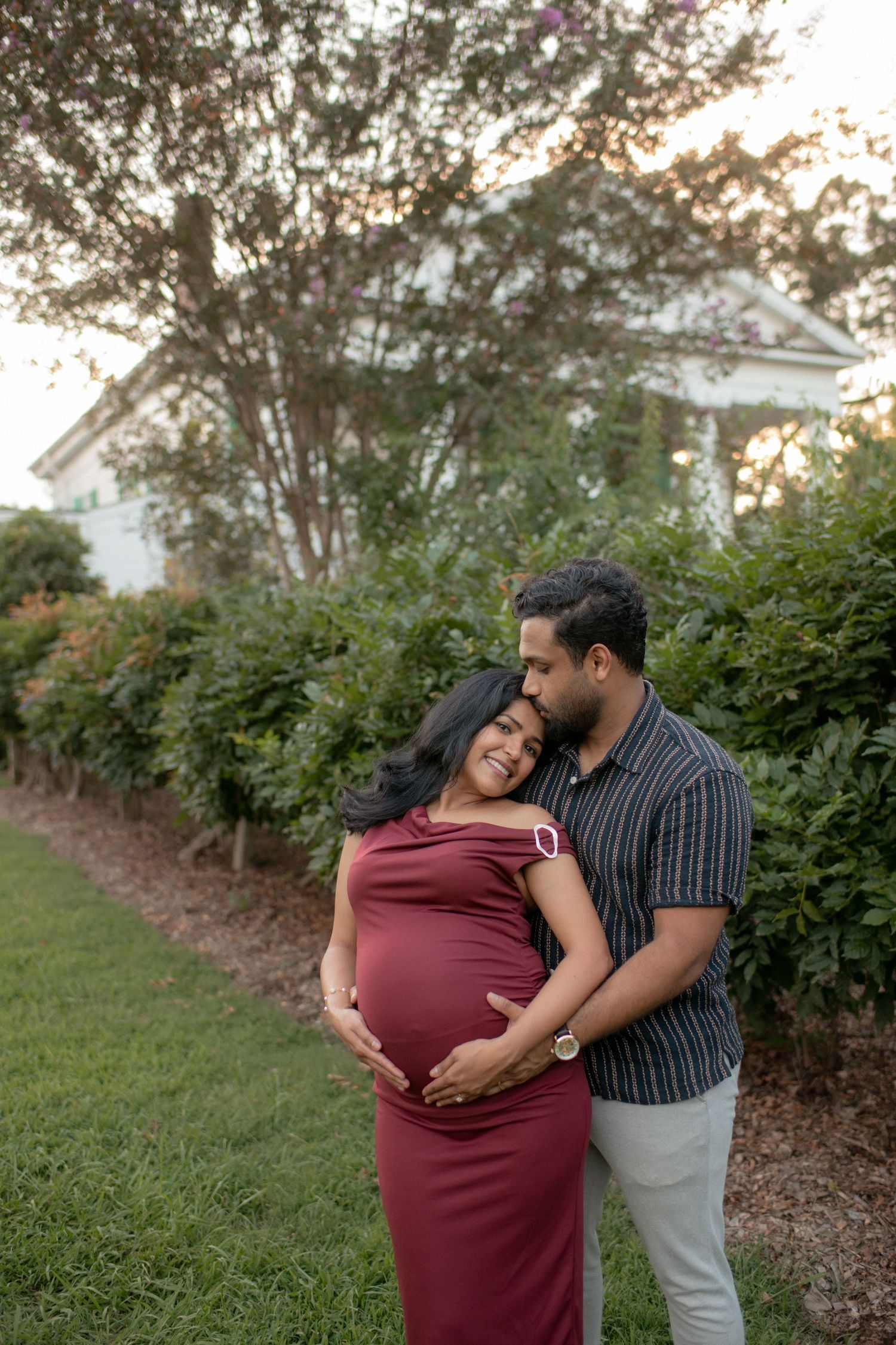 A couple shares tender moments during their maternity photoshoot in an outdoor garden setting.