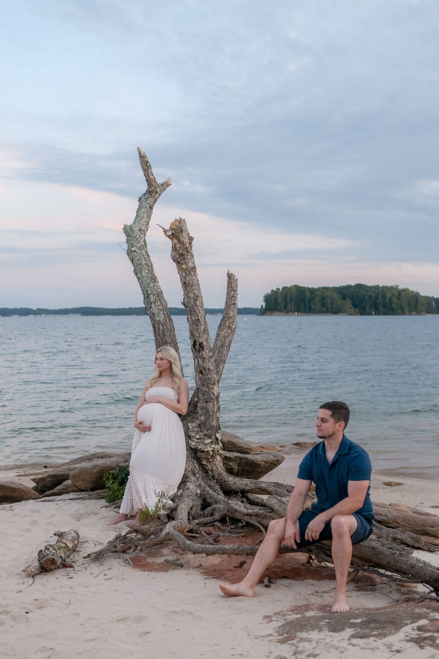 A couple sits together on driftwood at the beach during sunset.