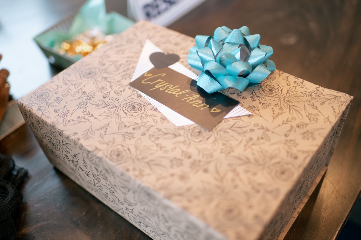 A gift box wrapped in patterned silver paper topped with a decorative blue bow sits on a dark surface.