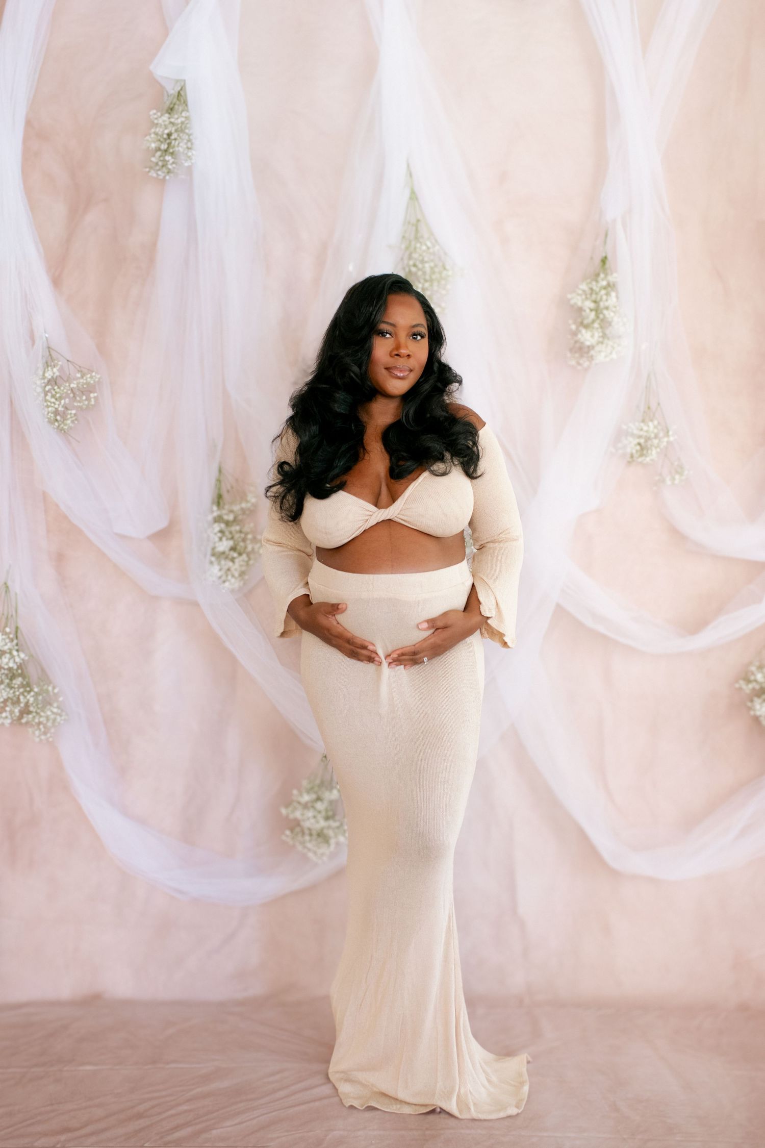 Maternity photos in white against flowing fabric backdrop showing a pregnant woman's silhouette.