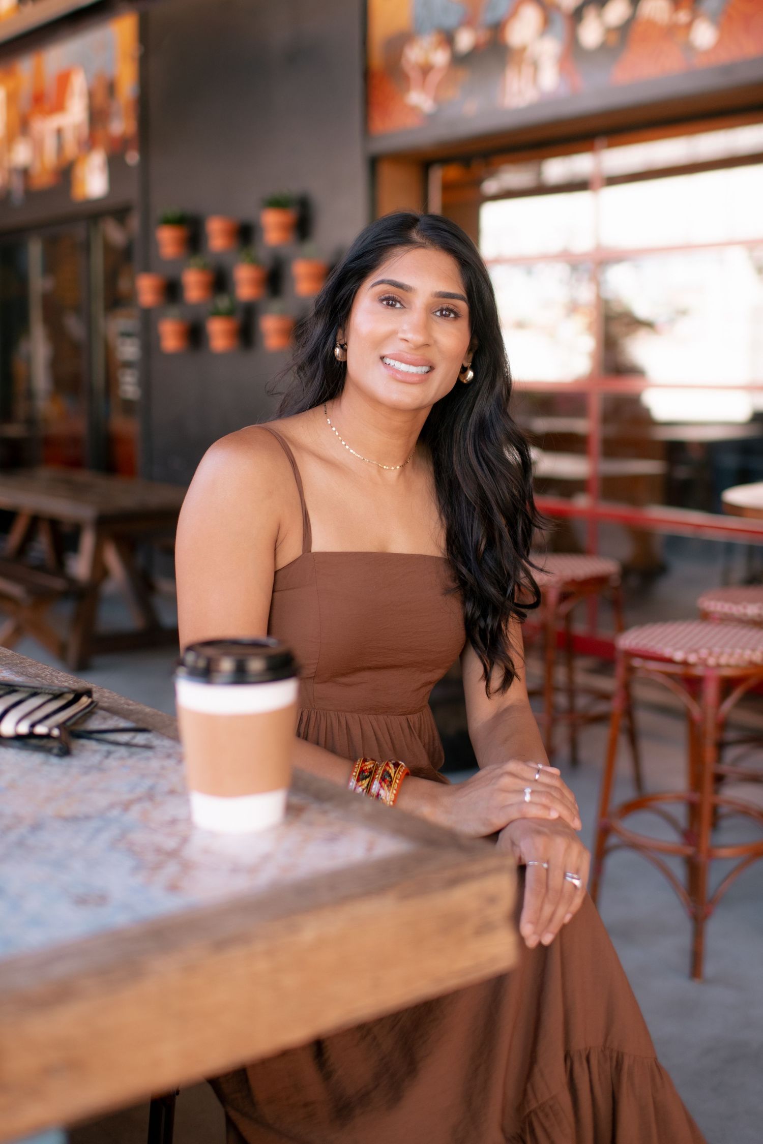 A woman in a brown dress sits at a wooden table in a cafe with warm lighting and rustic decor.