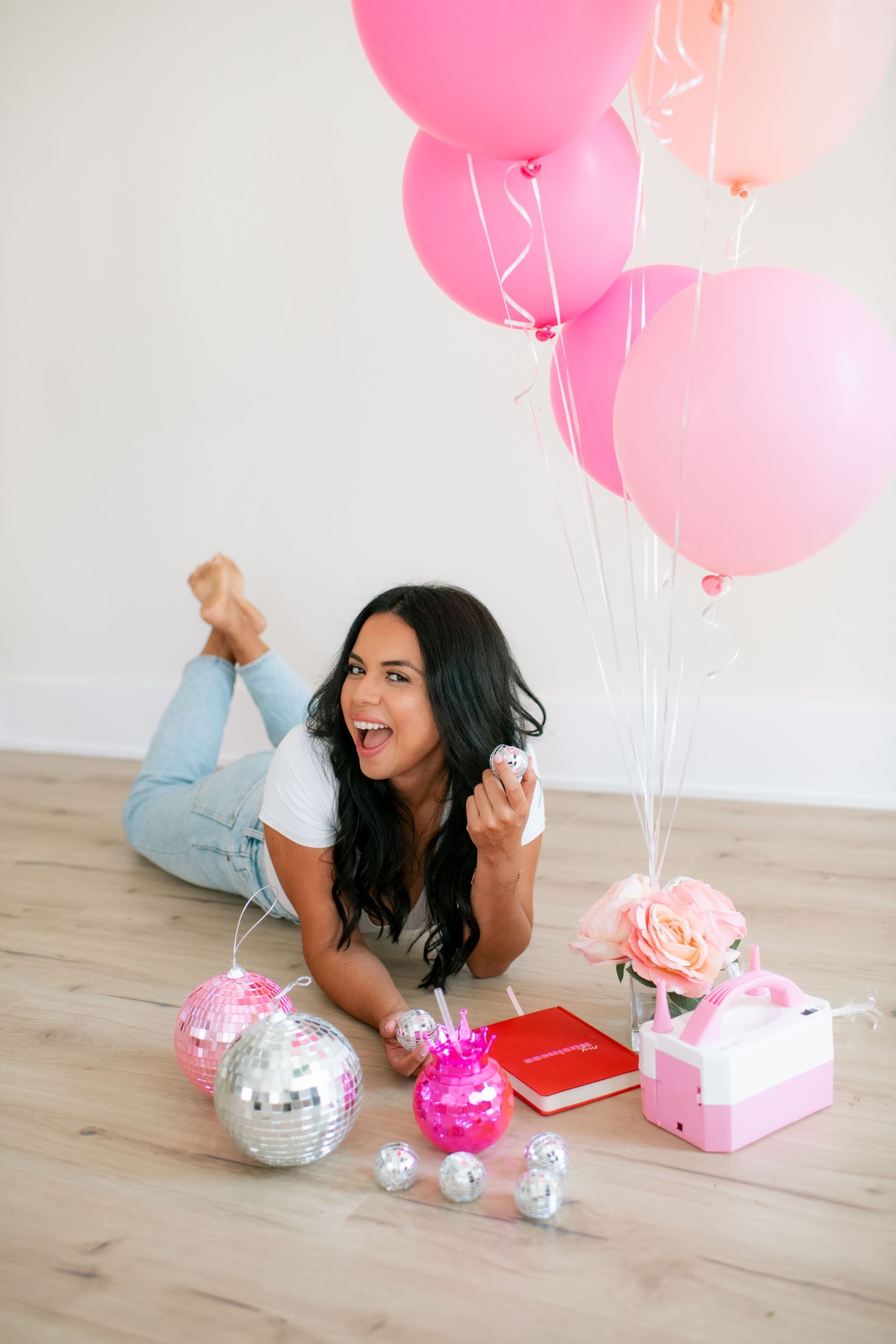 Decorative scene with pink balloons, sparkly disco balls, and wrapped presents on wooden floor.