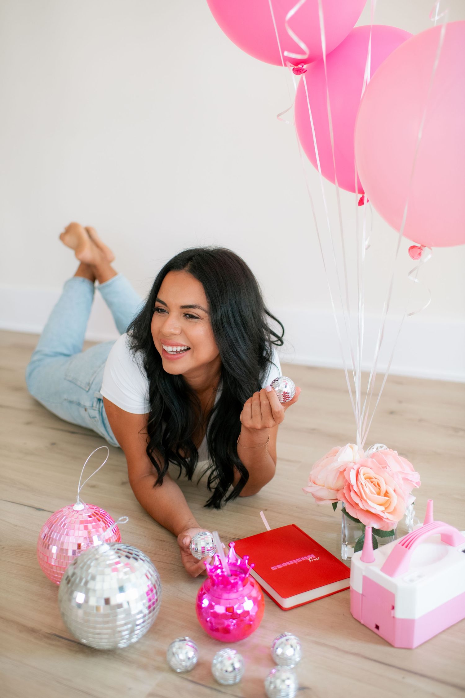 Pink balloons and silver disco balls create a playful scene with decorative elements on a wooden floor.