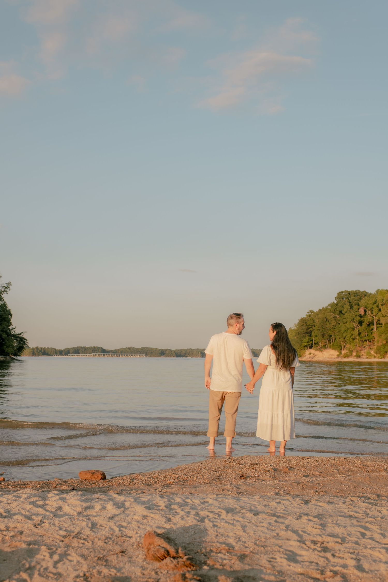 Couple walking hand in hand along peaceful beach shoreline at sunset.