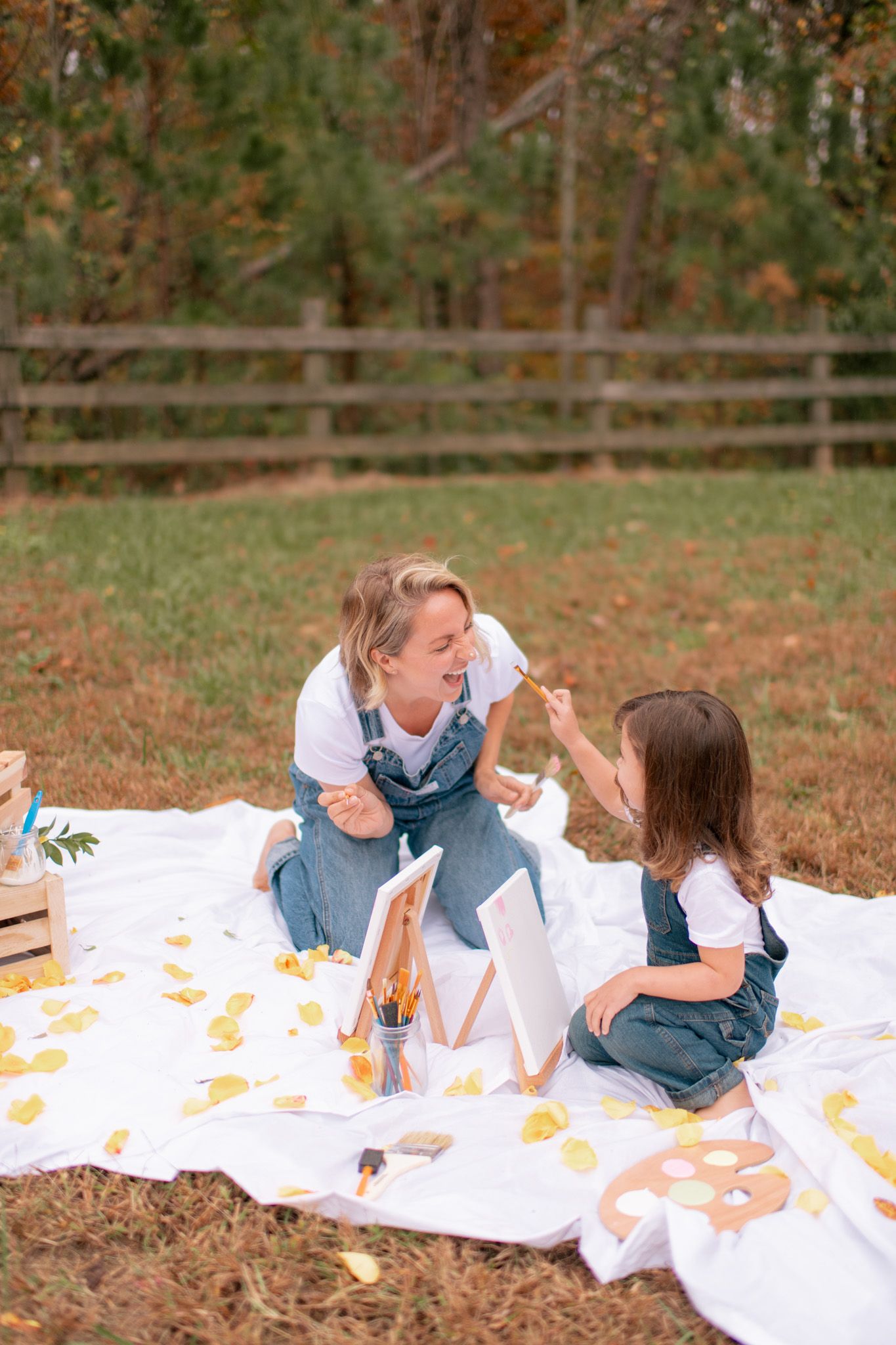 Three friends share laughter while lying on a white blanket scattered with autumn leaves in a park setting.