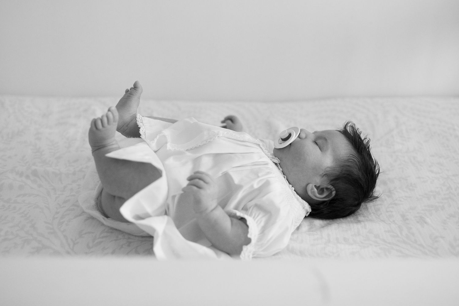 Black and white portrait series of a sleeping newborn in white clothing.