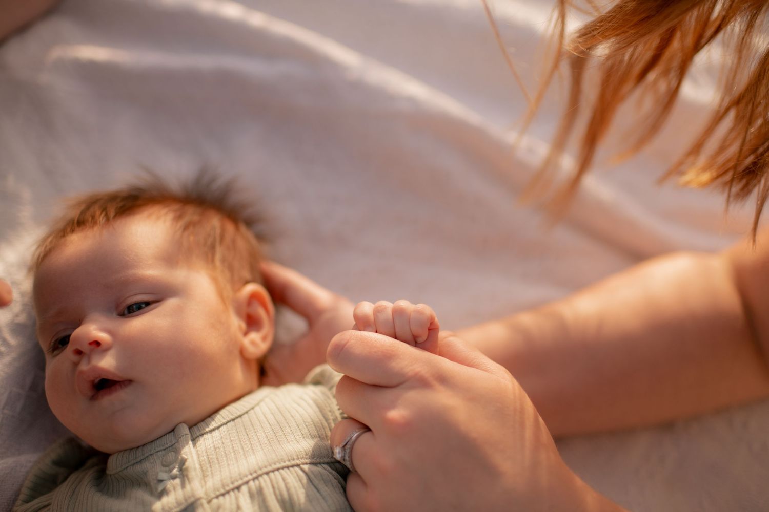 A gentle hand reaches out to touch and comfort a small baby lying in soft lighting.