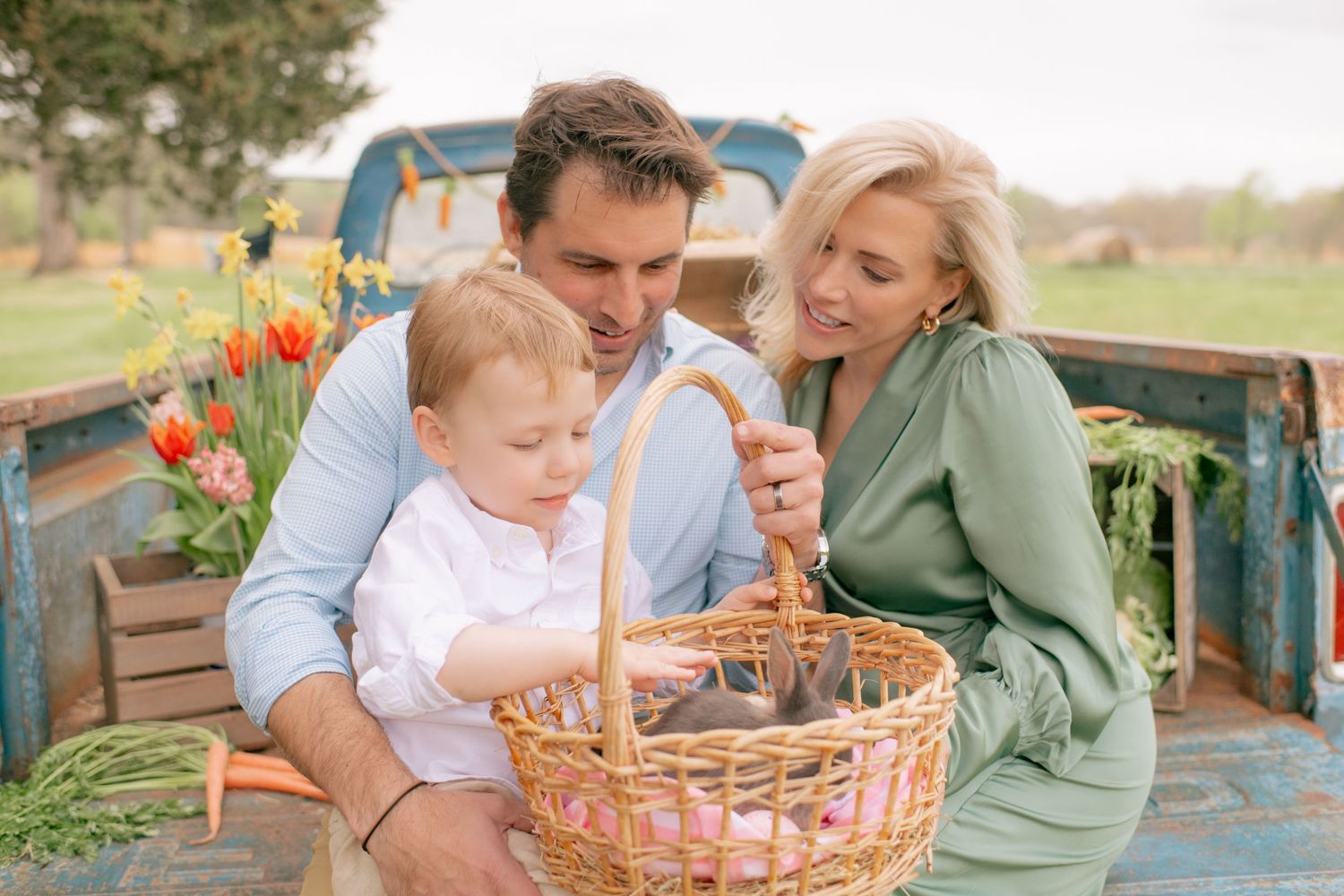 Three people sitting in vintage truck bed looking at Easter basket filled with colorful eggs and tulips in spring.