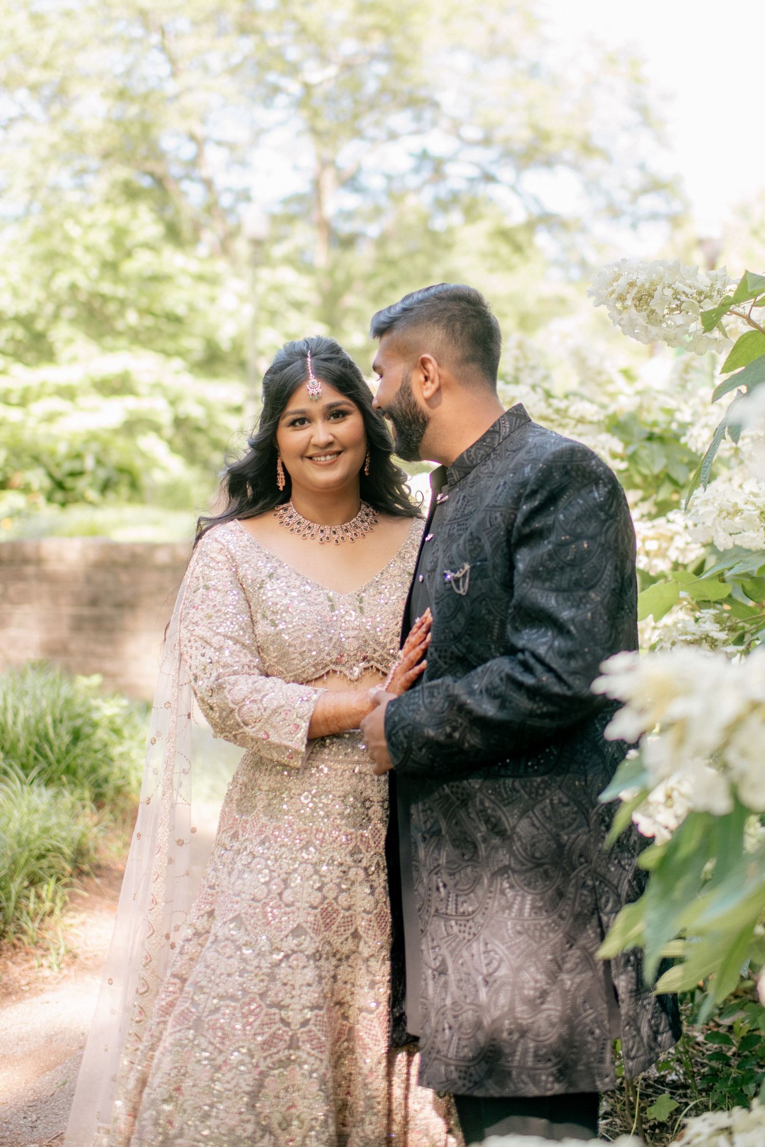 A romantic couple shares intimate moments in a garden setting wearing formal attire with pink blossoms in the background.