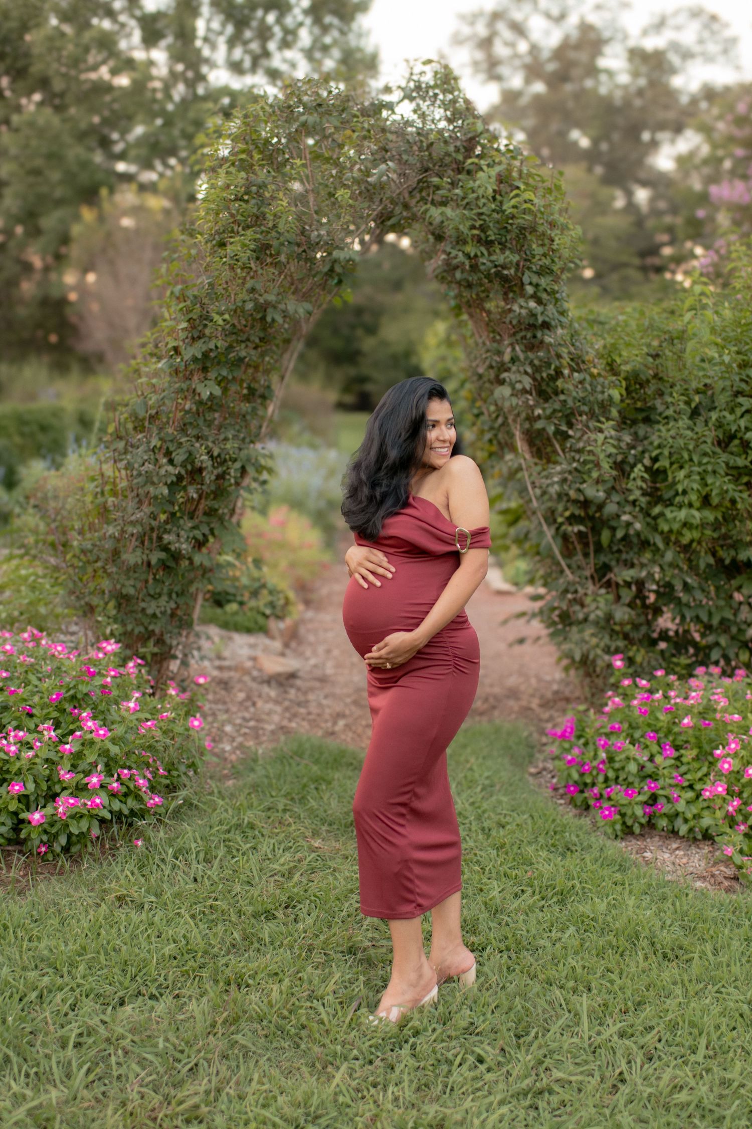 A couple embraces in a garden setting with pink flowers blooming in the background.