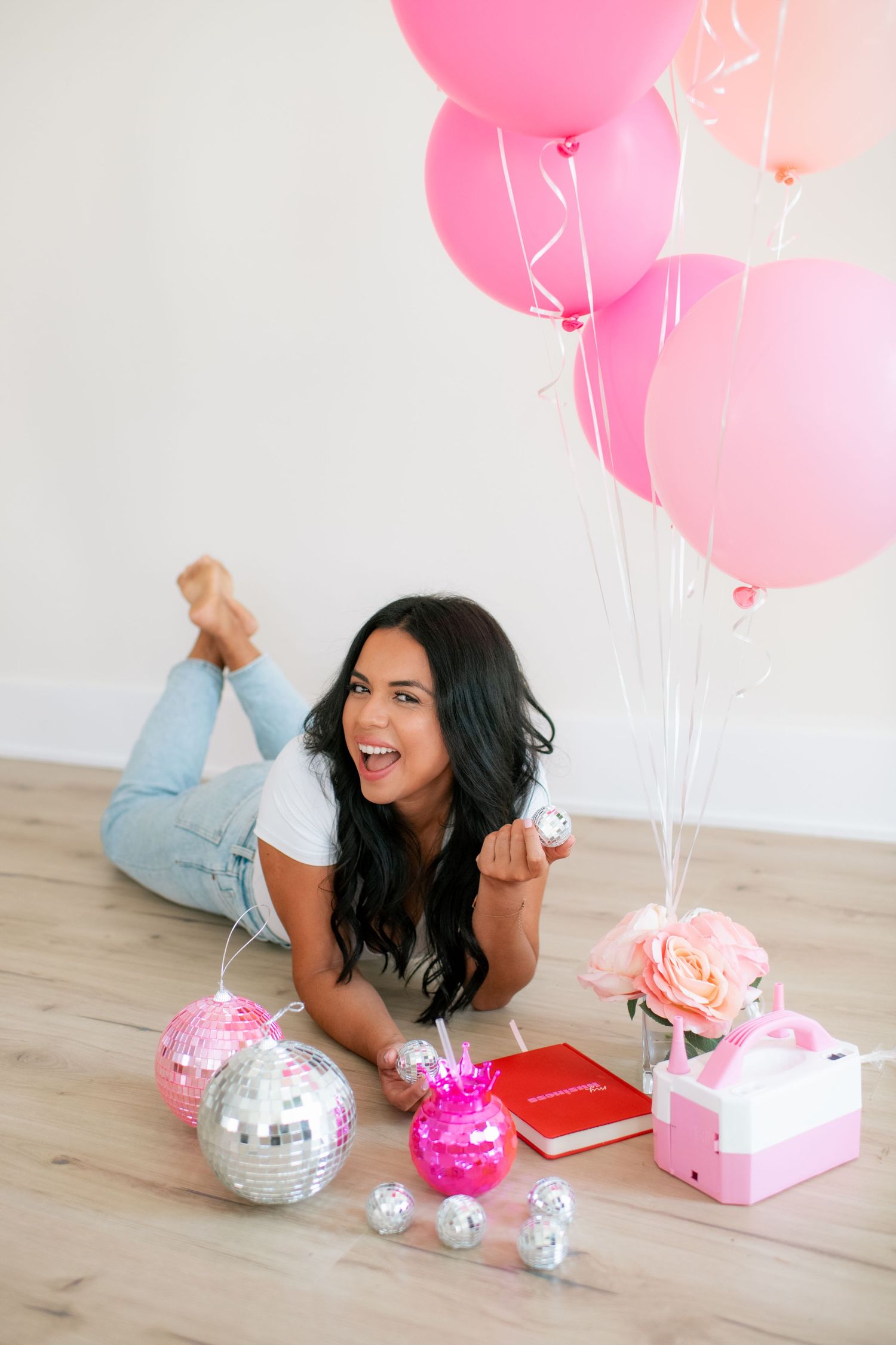 Decorative flat lay with pink balloons, disco balls and notebooks on wooden flooring.