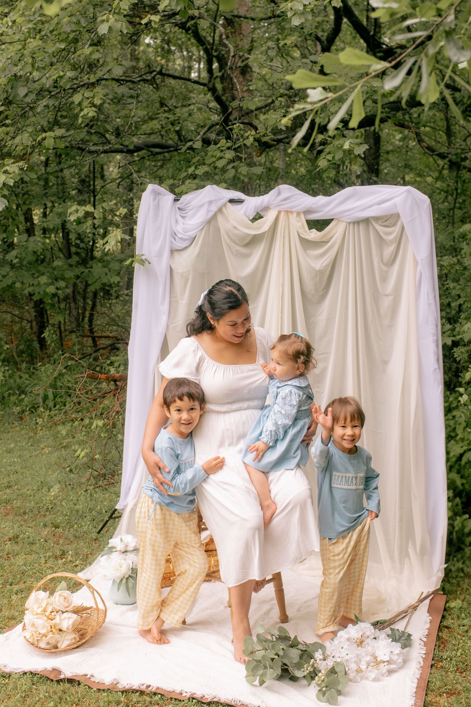 White flowy fabric backdrop provides dreamy outdoor setting for family photoshoot with floral accents and rustic basket props.