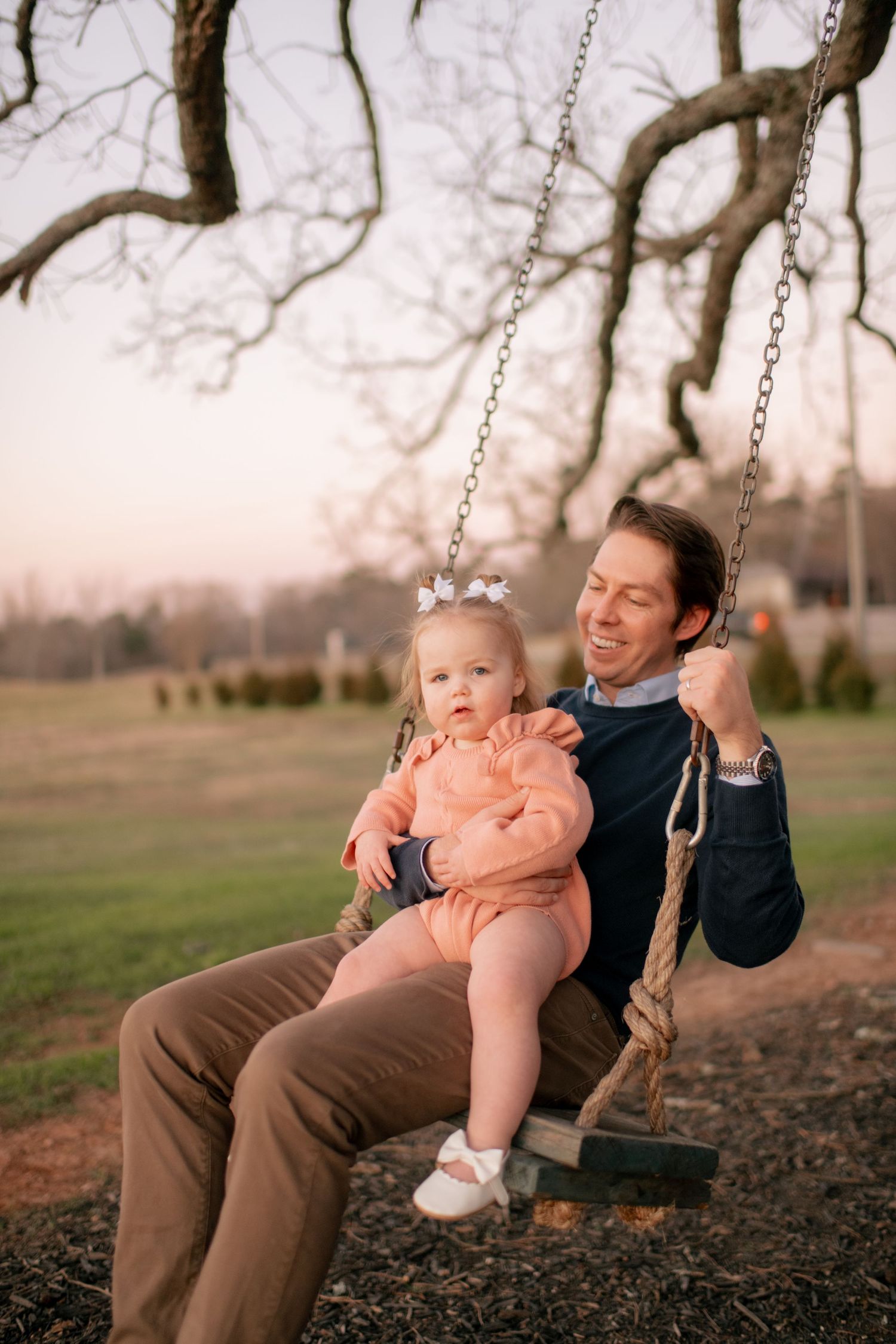 Parent and young child share joyful moment together on outdoor tree swing at dusk.