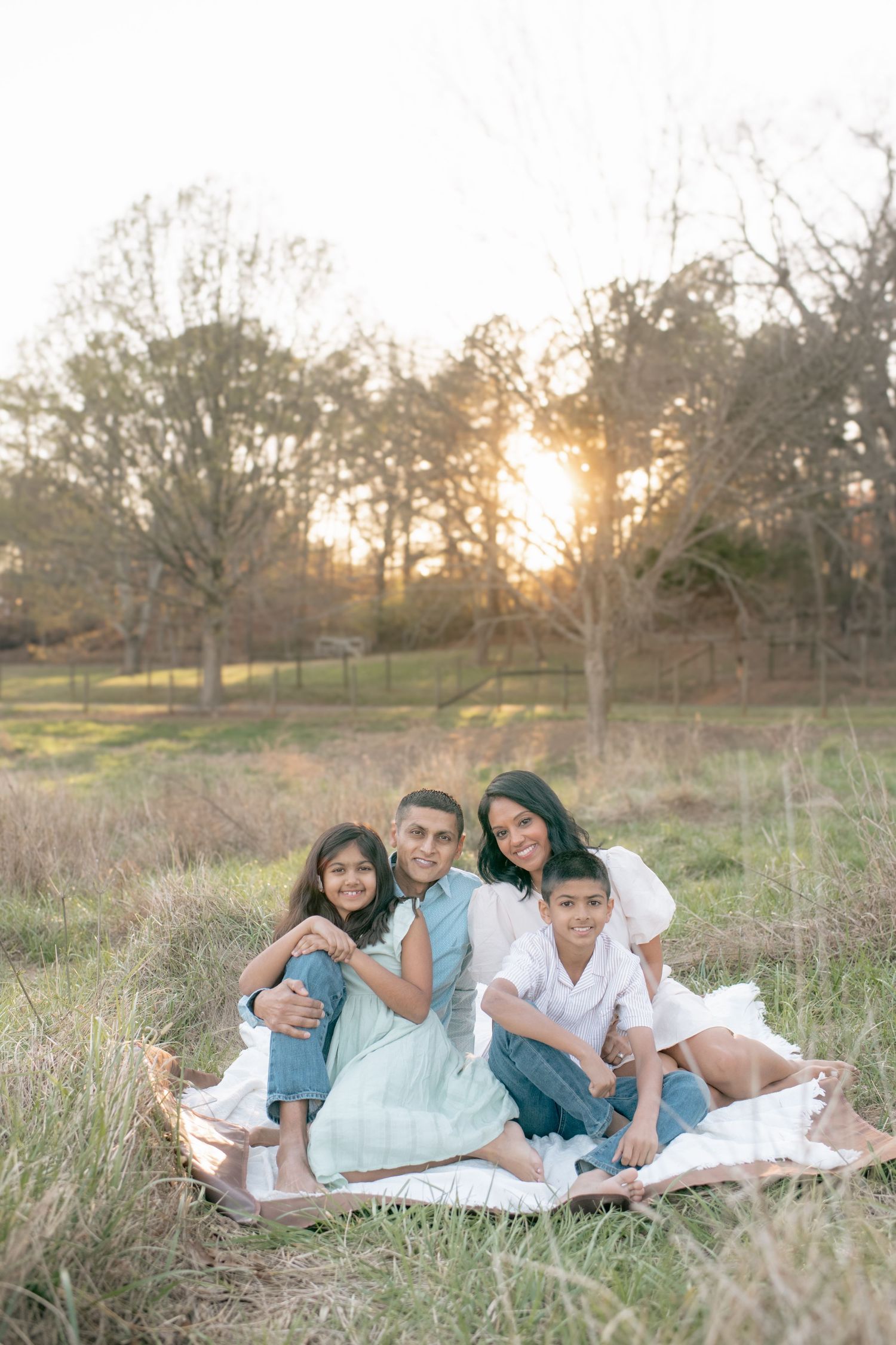Sunset family portrait in a golden meadow with a blanket on the grass during magic hour.