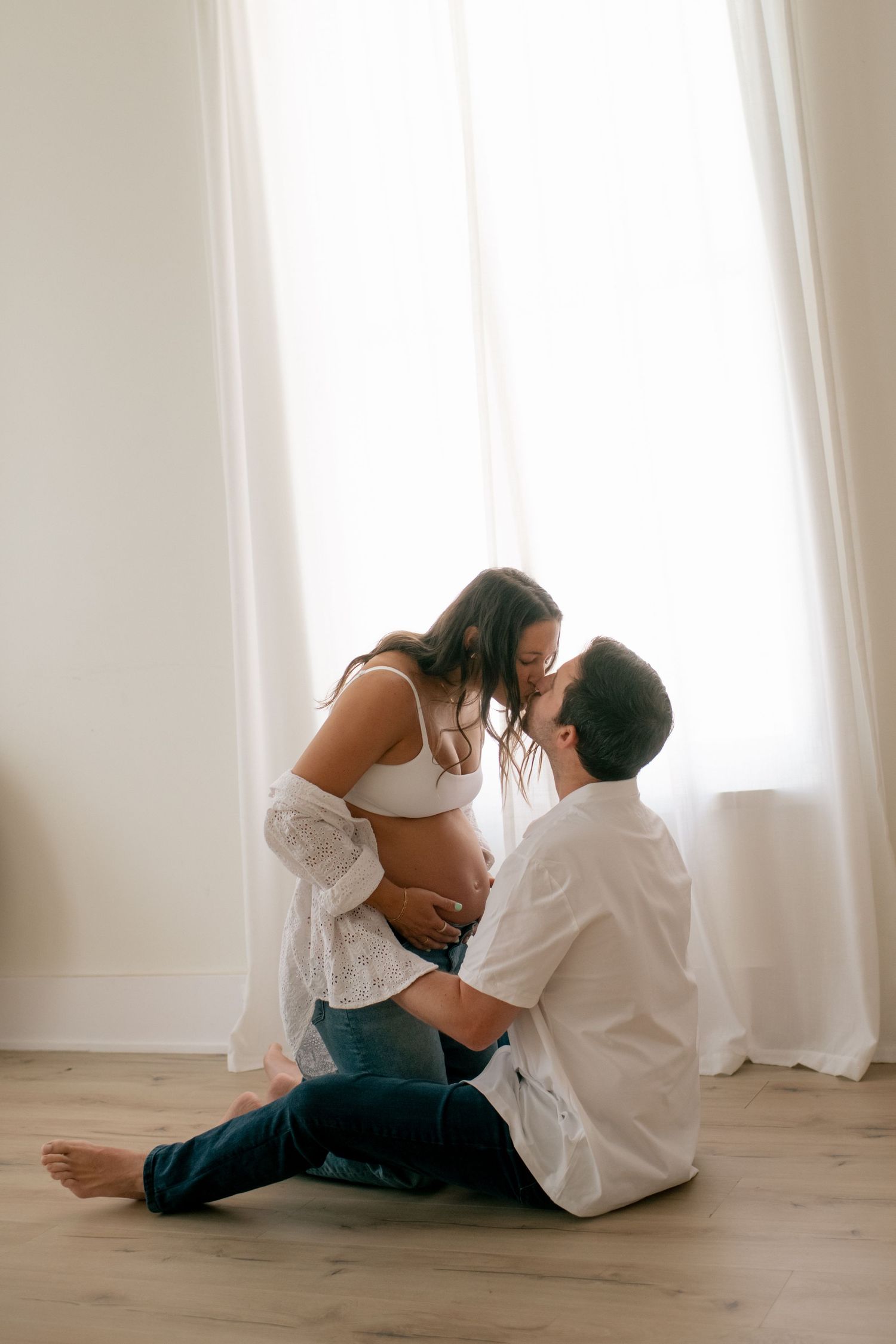 Intimate maternity session showing couple's tender moments on wooden floor.