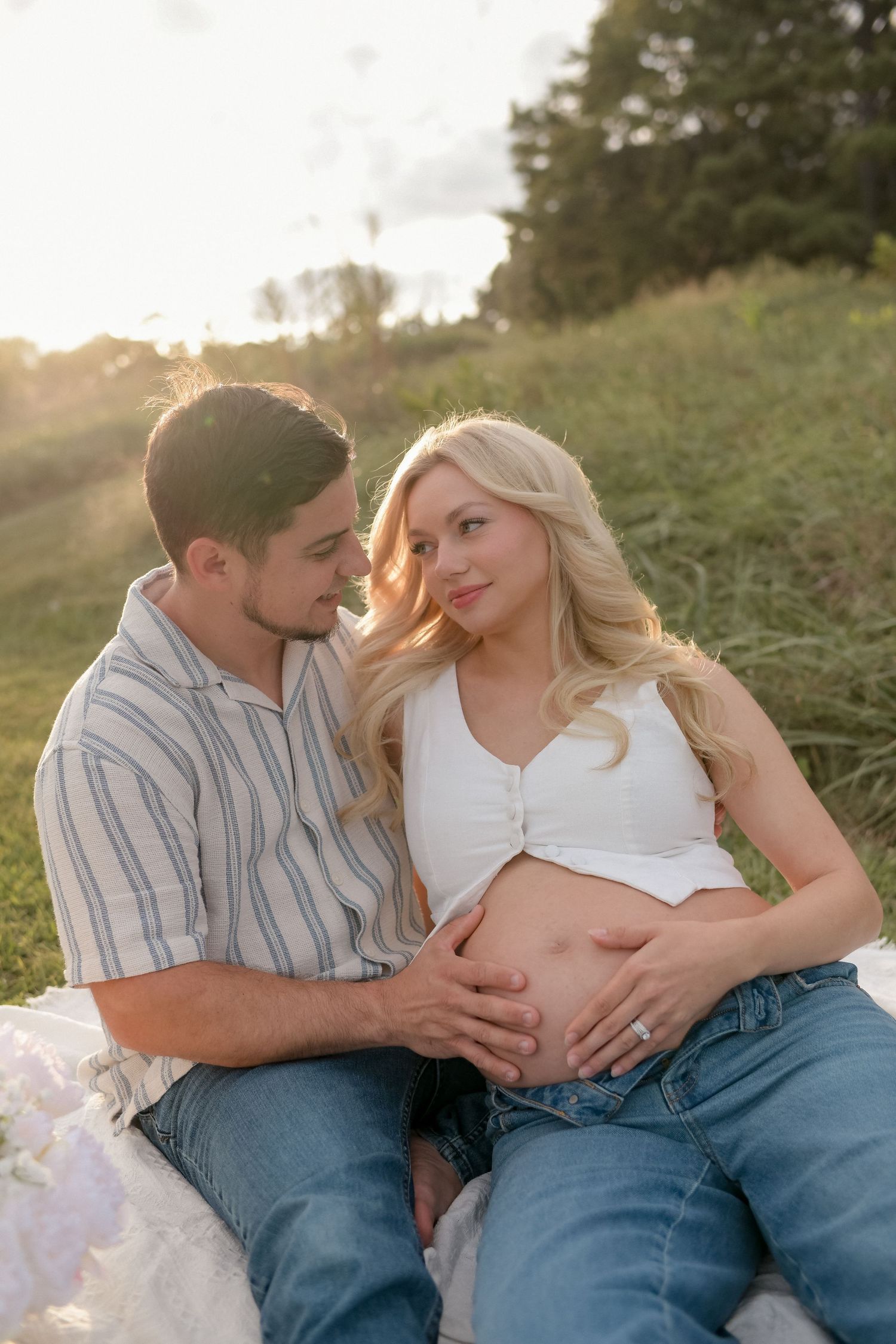Couple sitting together on a hillside during golden hour maternity photo session.
