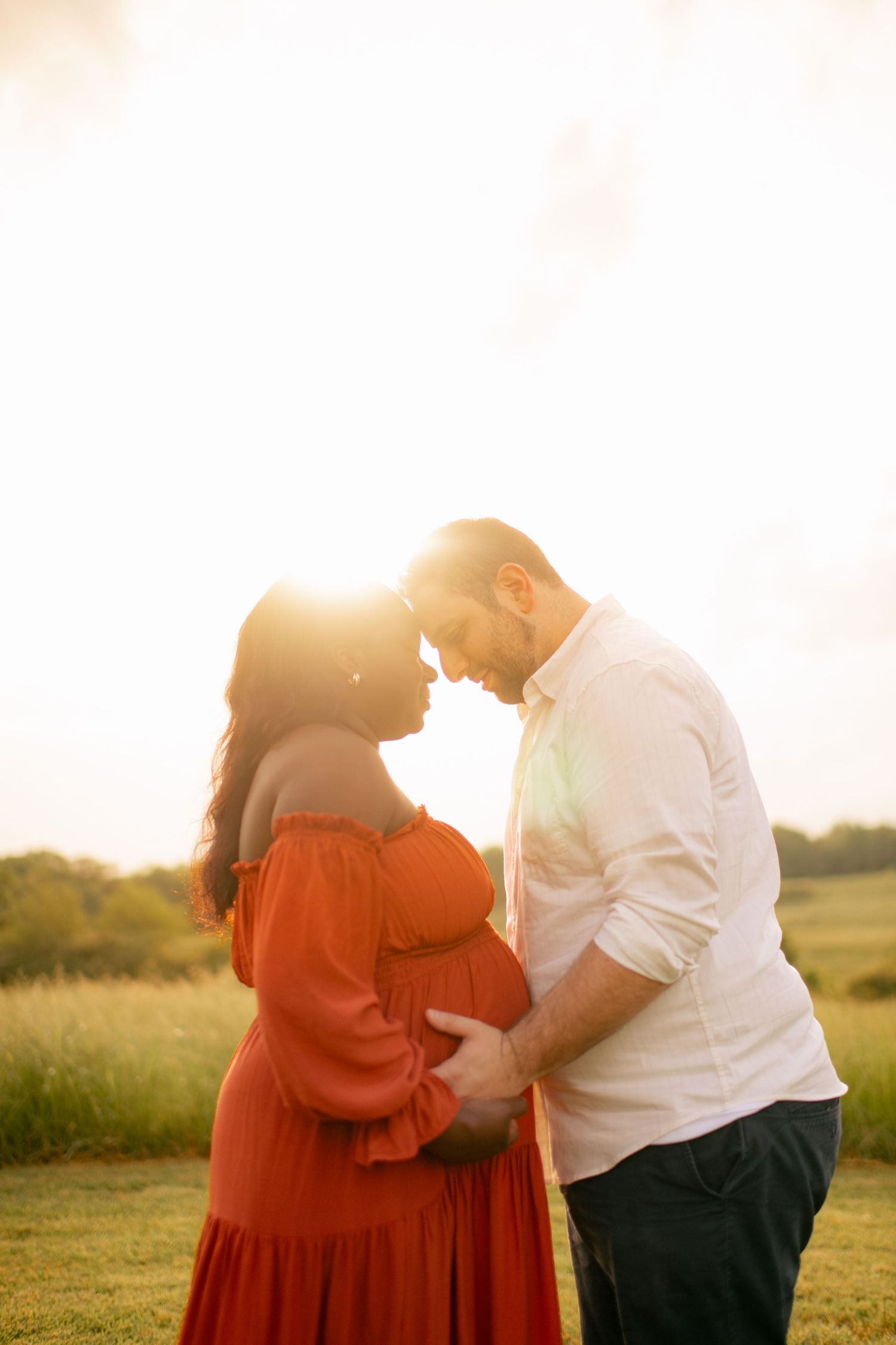 Couple embraces in a golden sunset field wearing red and white outfits.