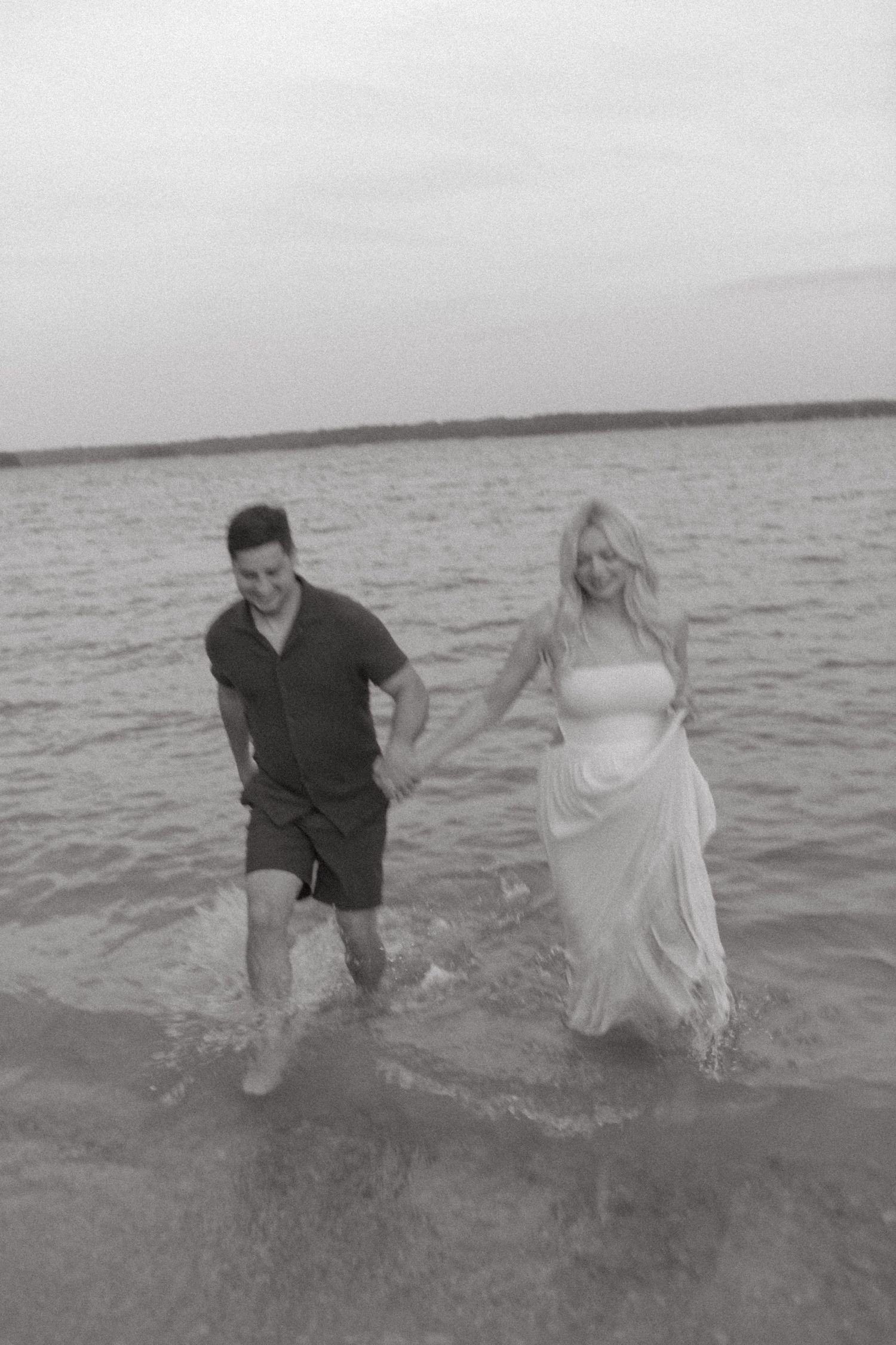 A couple plays and splashes together in shallow ocean water at sunset.