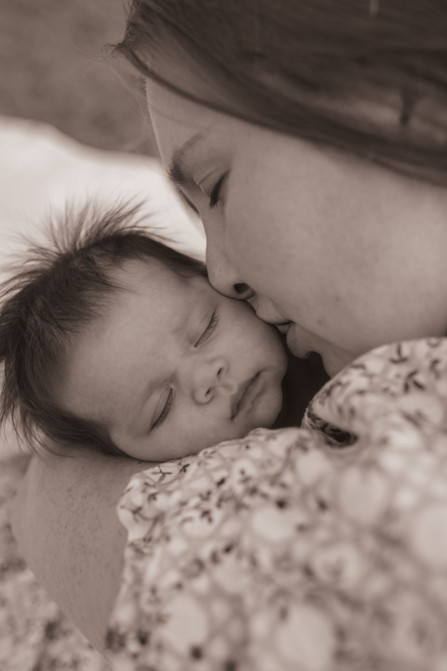 A tender black and white close-up photo shows a gentle loving moment between parent and sleeping baby.