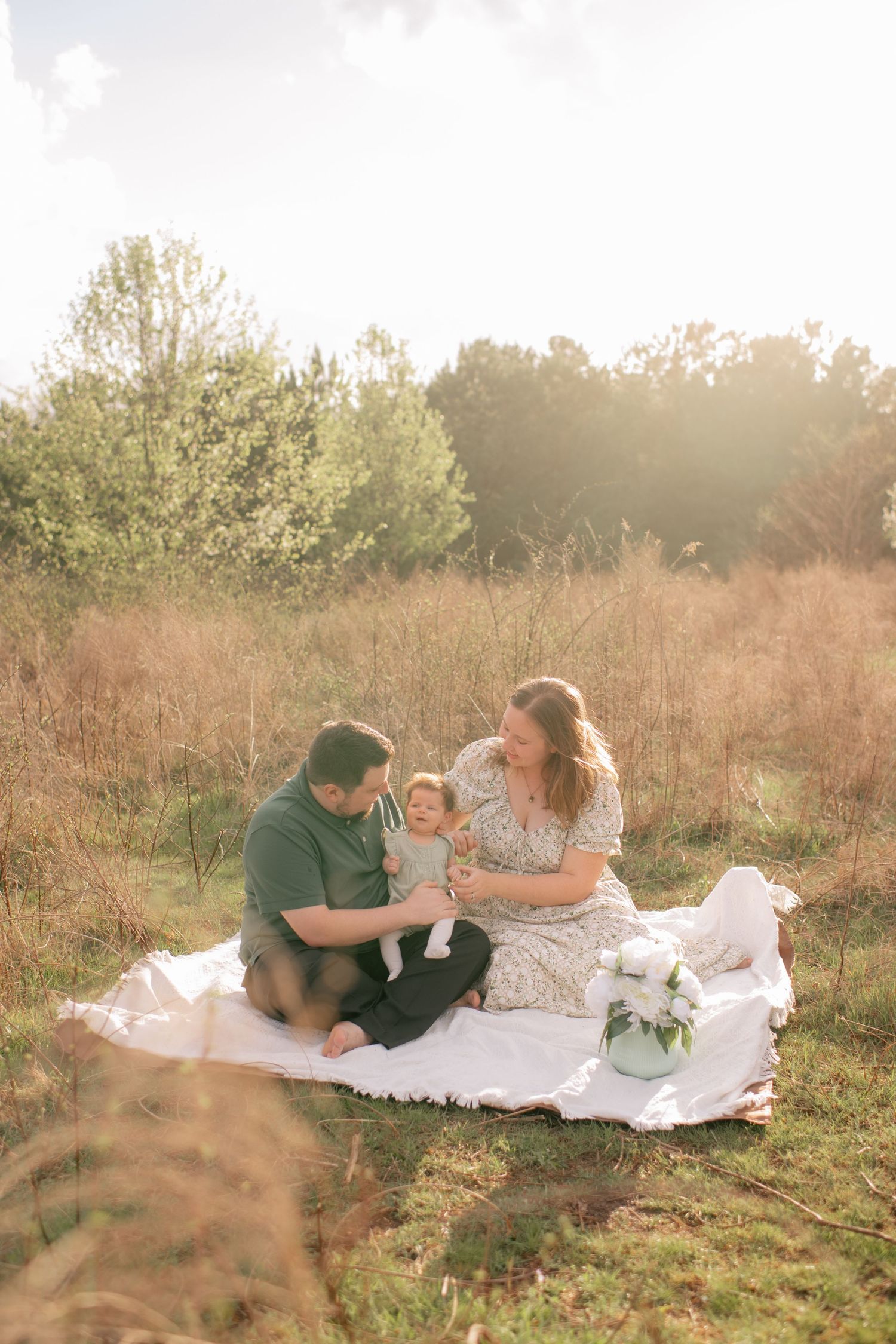 Family enjoying a golden hour picnic together on a white blanket in a sunlit autumn field.