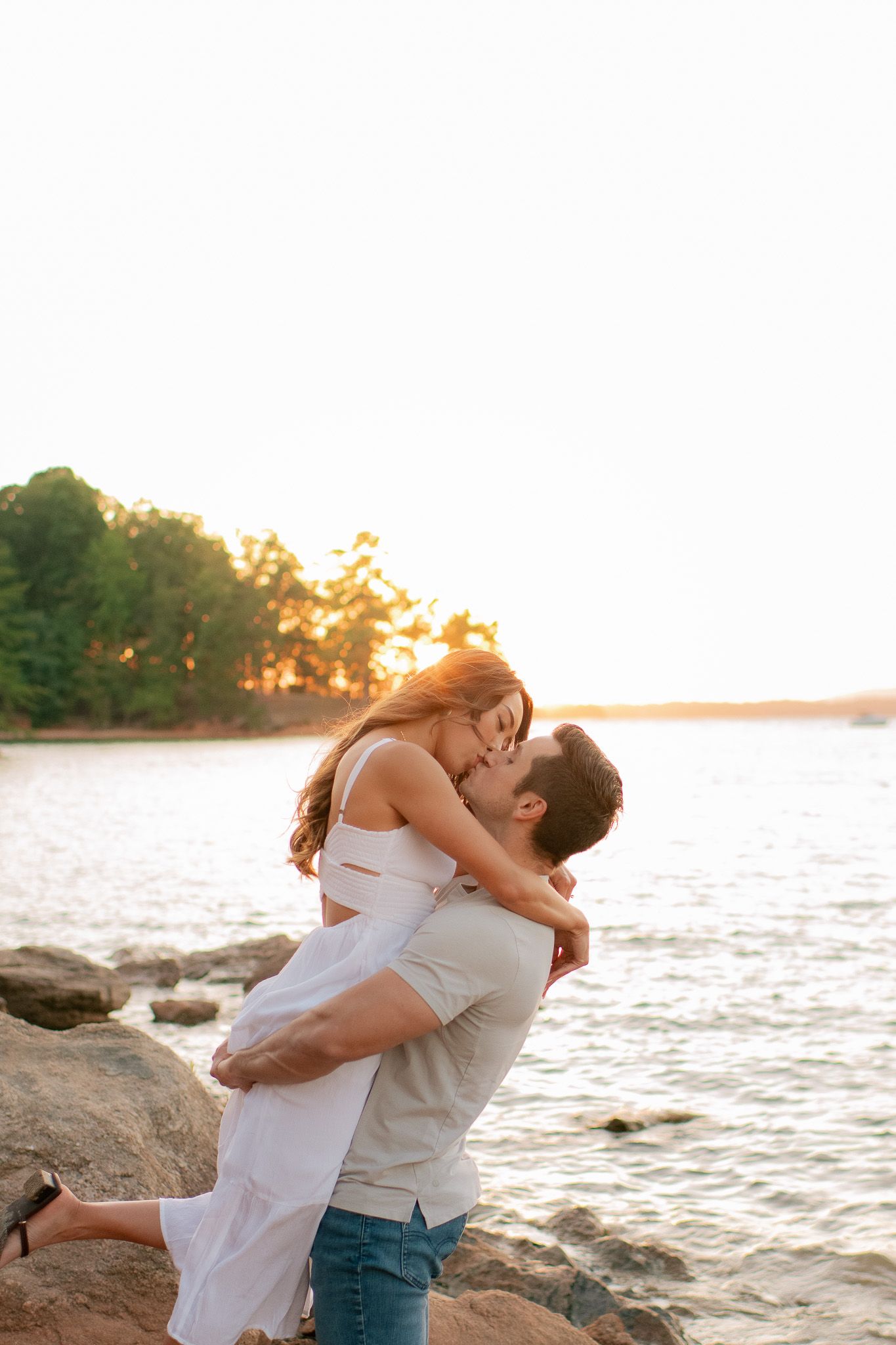 Two people embrace lovingly on a beach at sunset near the rocky shoreline.