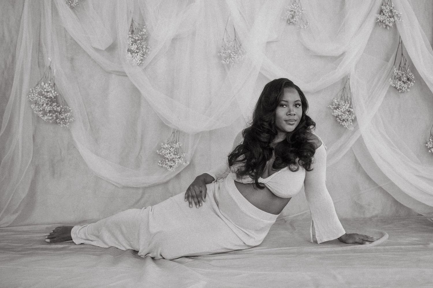 Black and white maternity photo with elegant pose on draped fabric backdrop.