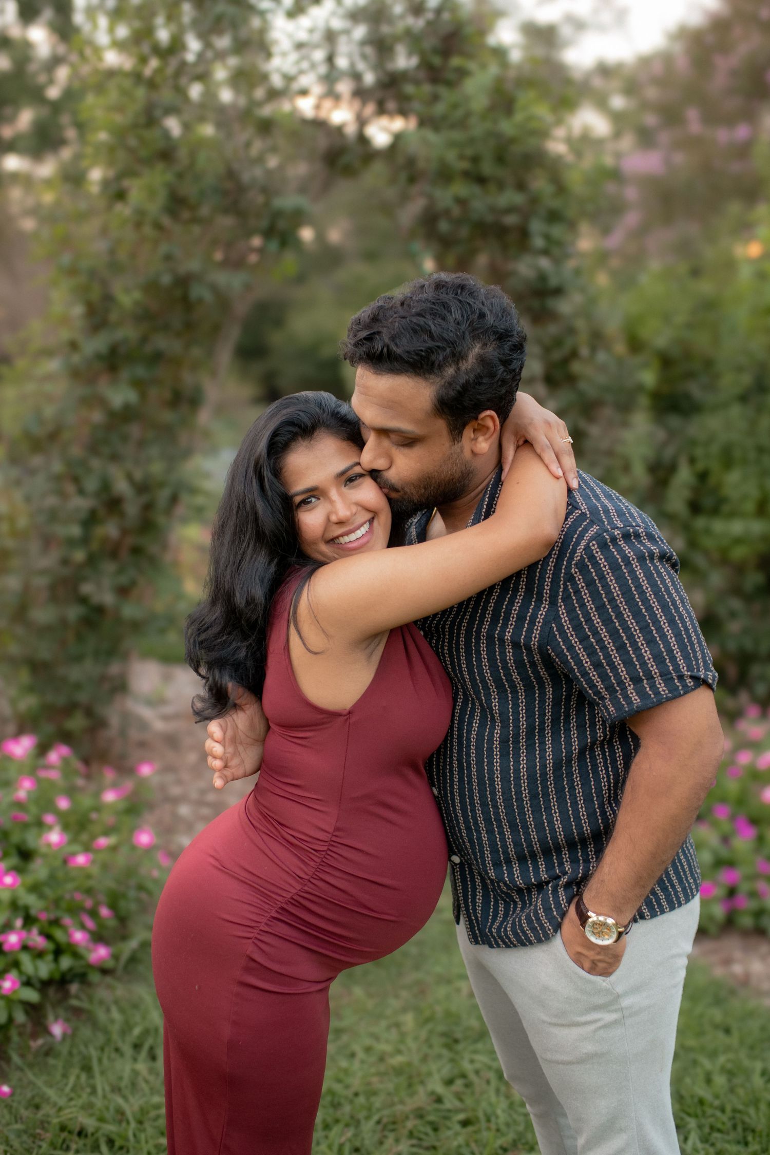 Playful maternity photoshoot in garden with pink flowers blooming.