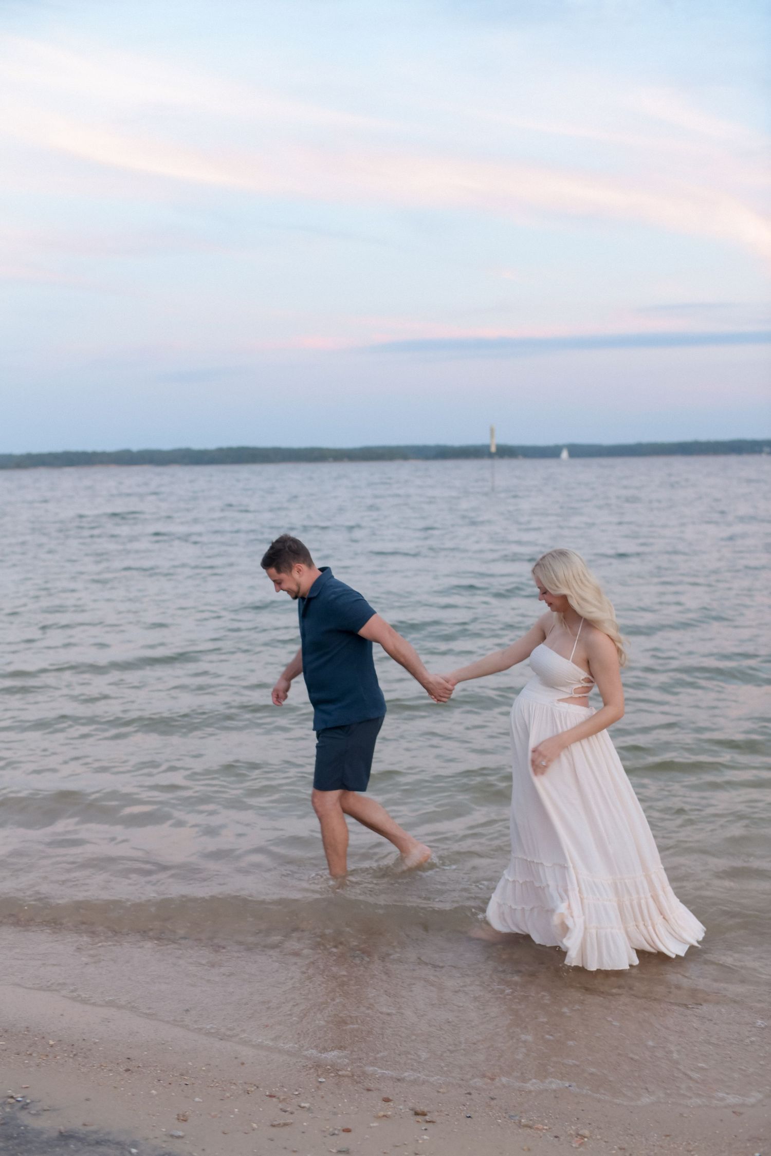 Playful couple walking along shoreline during sunset beach photoshoot.