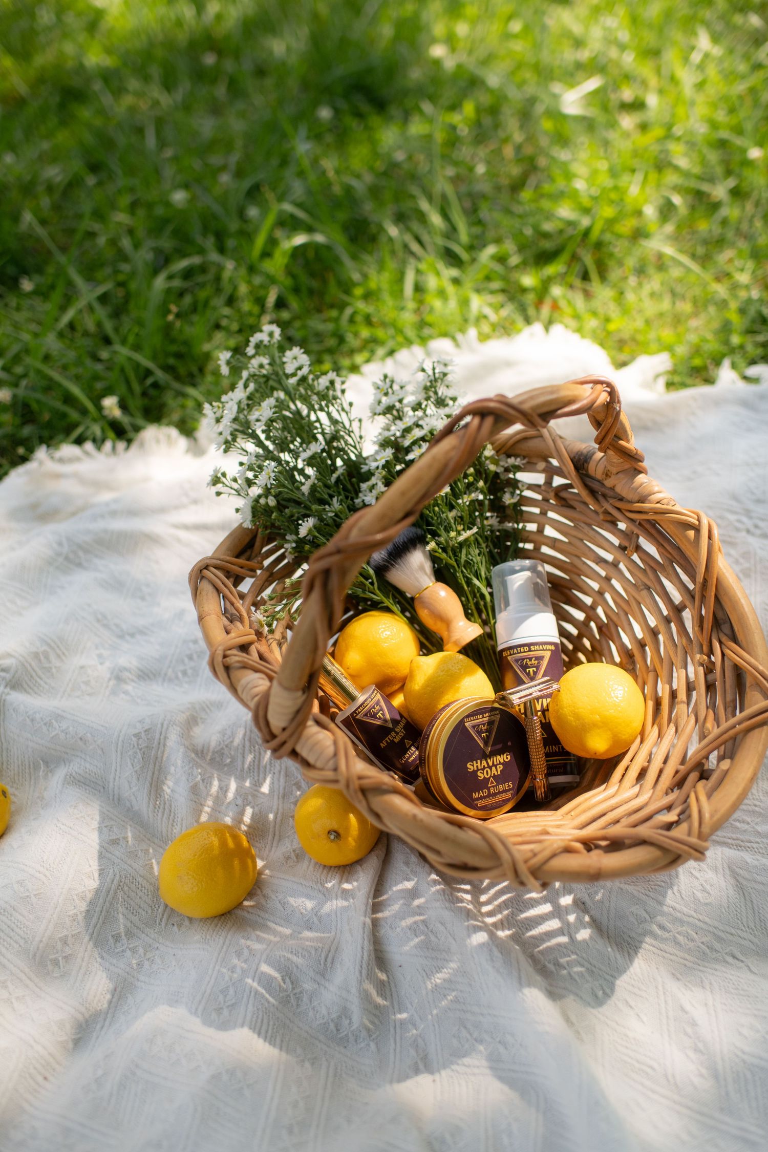 Wicker basket with lemons, skincare products, and herbs on a white blanket in a sunny garden.