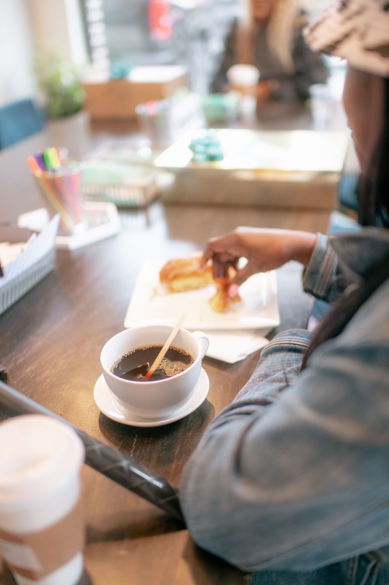 Person eating at a wooden table with white plates and dishes in a casual dining setting.