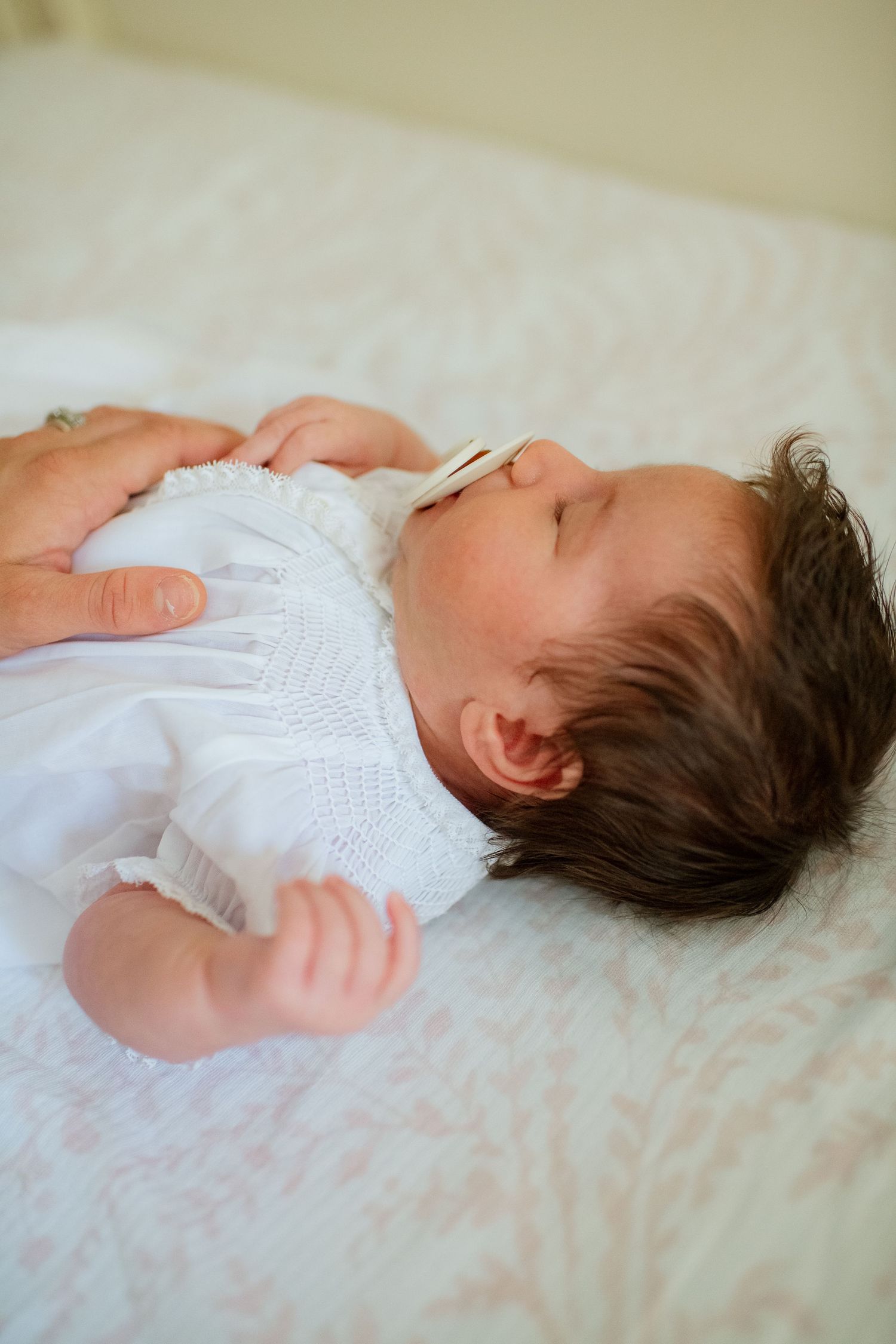 Newborn baby in white clothing lying peacefully on soft white bedding.