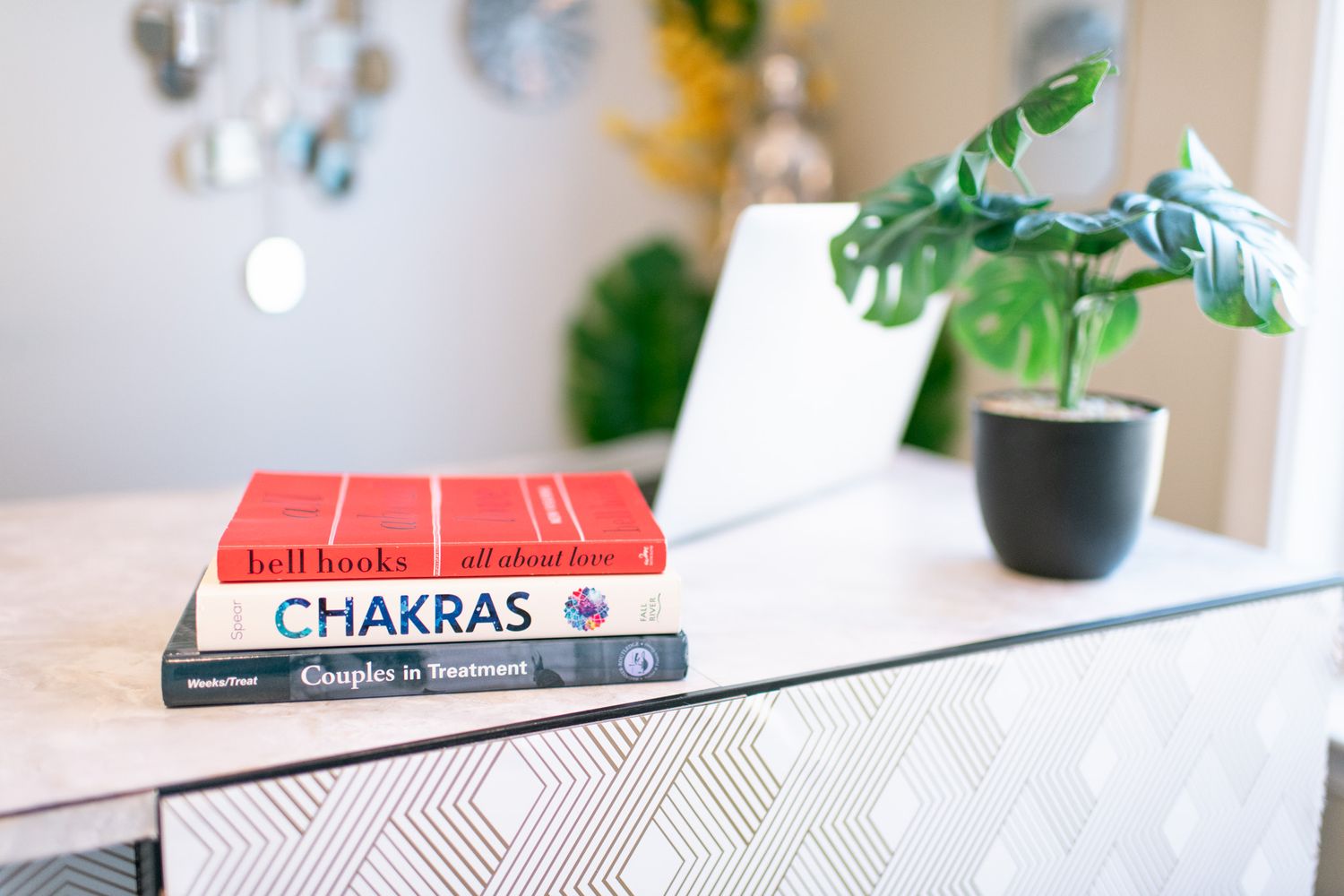 Stack of books on chakras and self-help topics displayed on a modern desk beside a green monstera plant.