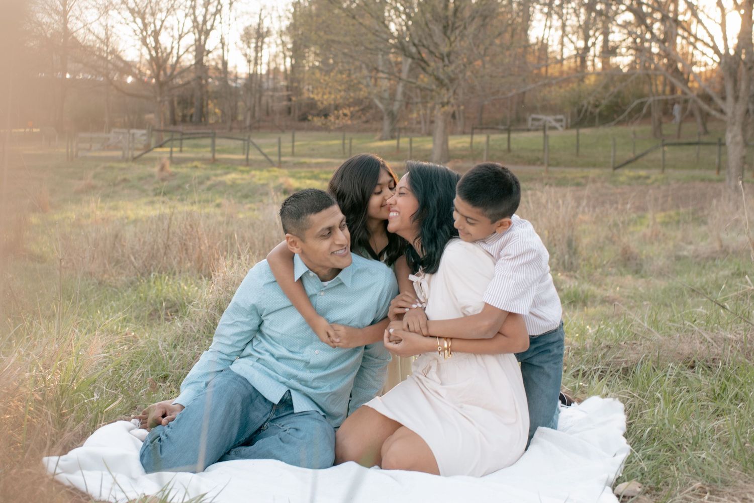 A group sits together on a white blanket in a sun-lit field during golden hour.