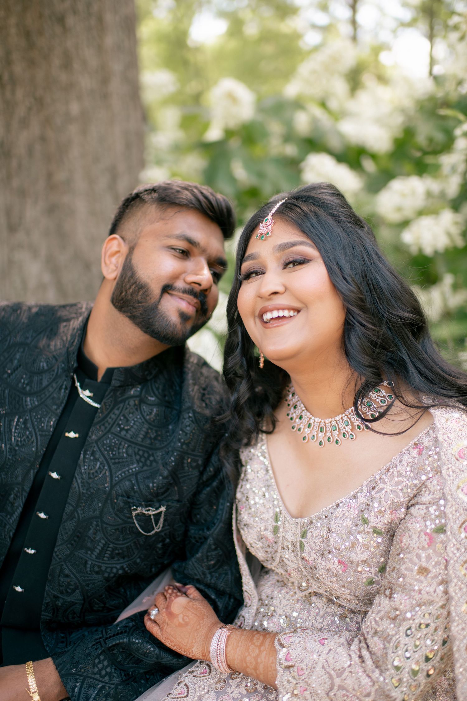 A joyful couple in traditional South Asian wedding attire share intimate moments during their outdoor photo session.