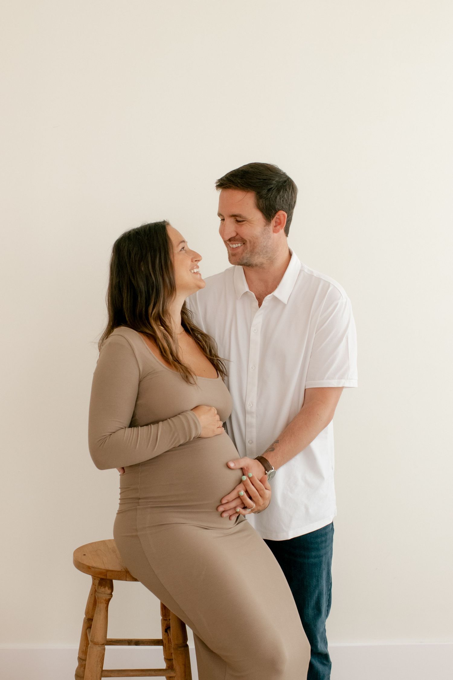 Couple sharing intimate moment during maternity photoshoot with wooden stool.