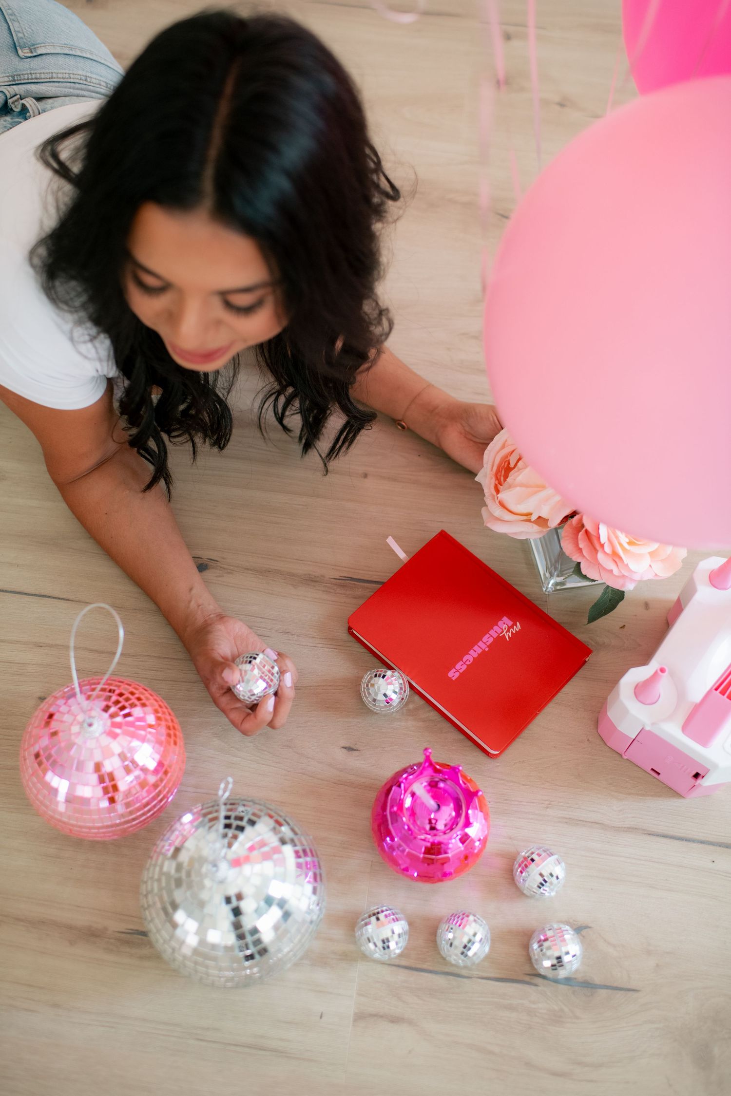 Close-up view of silver disco balls and pink party decorations arranged on a light wooden floor.