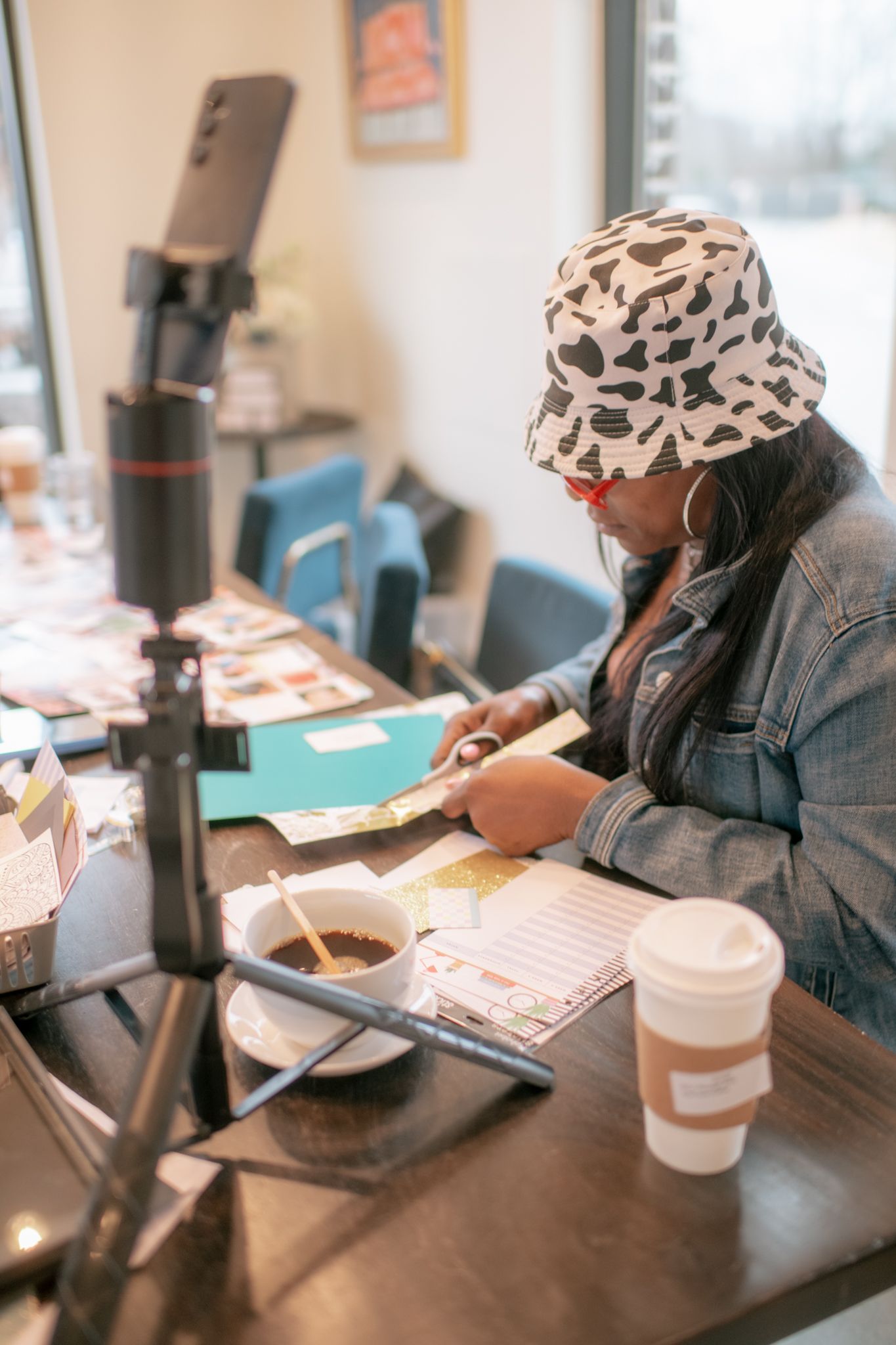 Someone wearing a patterned headscarf and denim jacket working at a desk with a coffee cup.