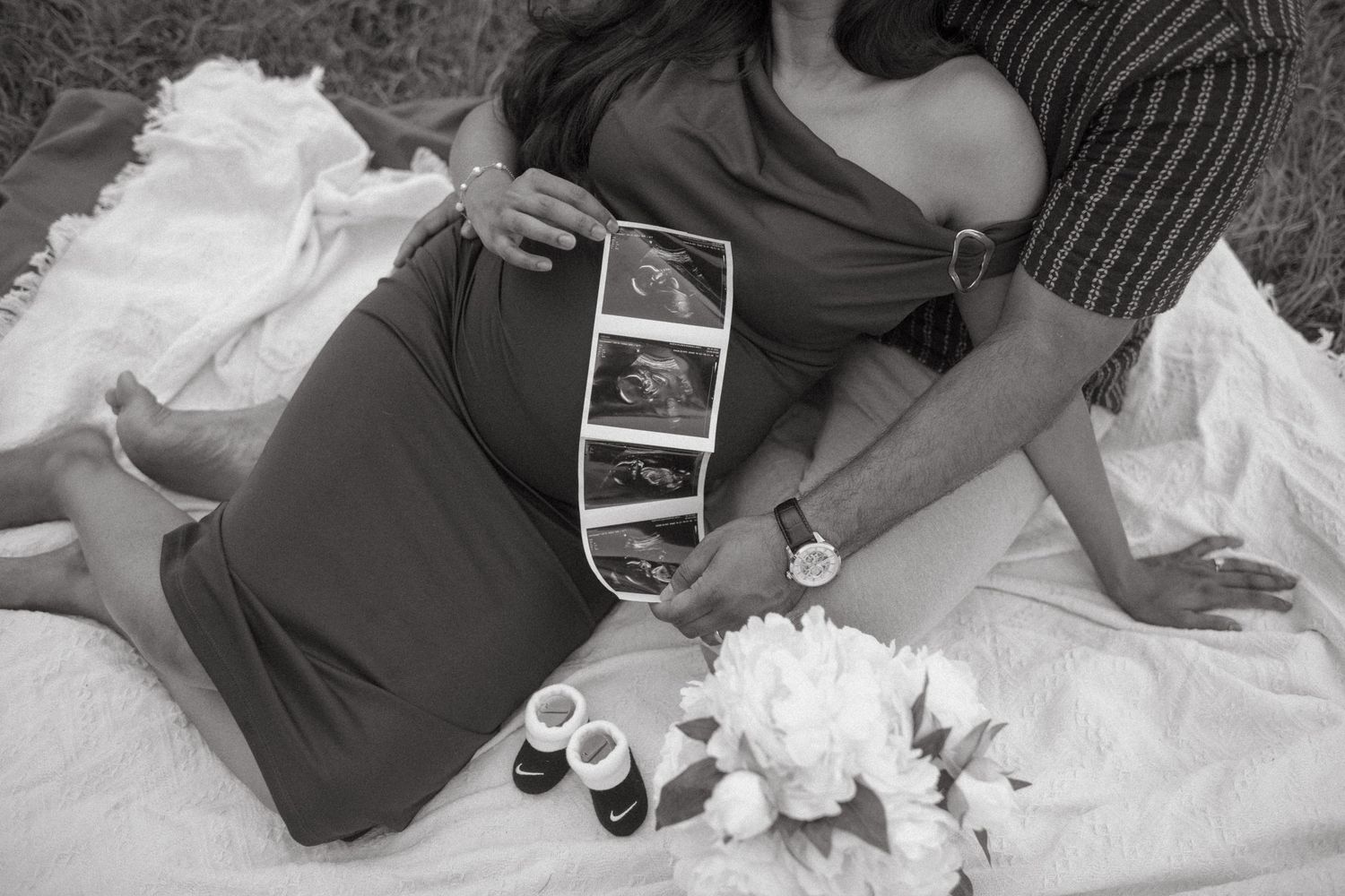 Black and white photo of a couple looking at ultrasound images while relaxing on a blanket.